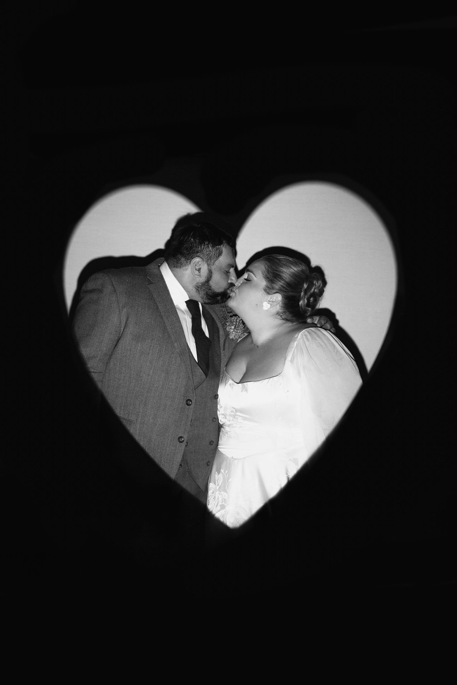 Black and white wedding photo of a couple kissing framed in a heart-shaped cutout.