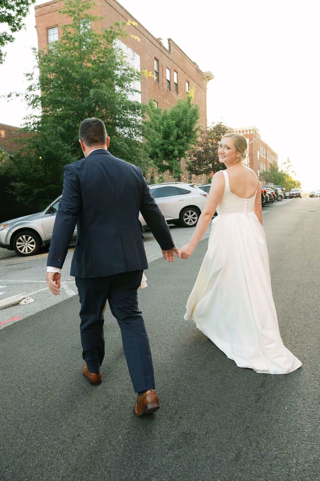 Wedding couple walks hand in hand down a quiet residential street at sunset.
