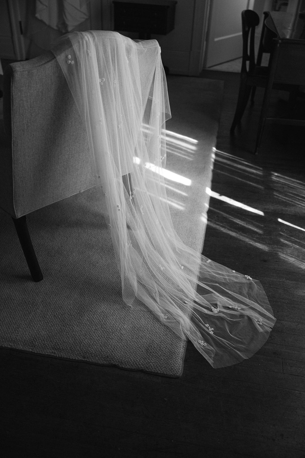 Black and white image of a flowing white veil draped over a chair with sunlight streaming across.