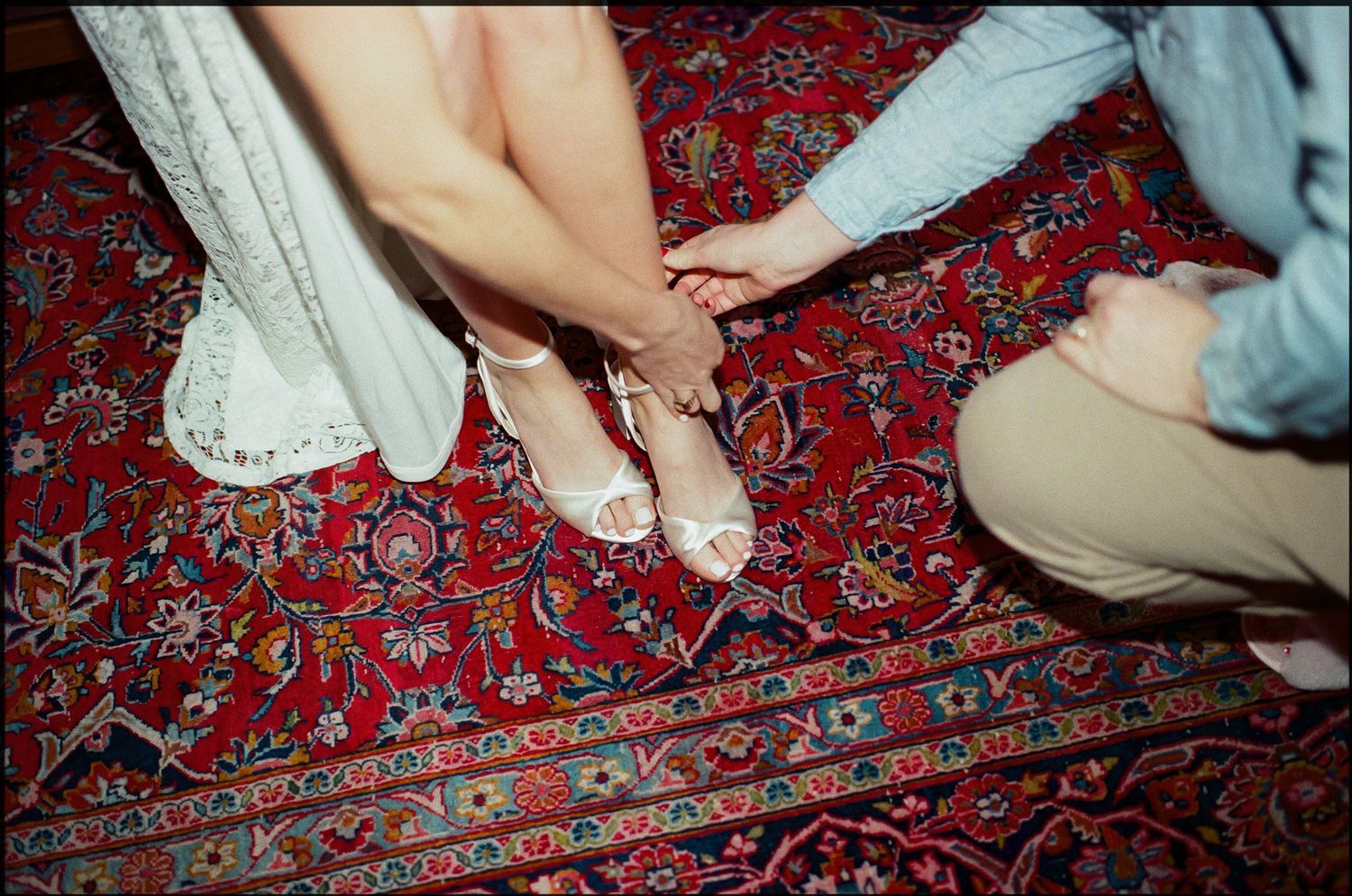 Guests' feet and legs shown on an ornate red patterned carpet at an event.