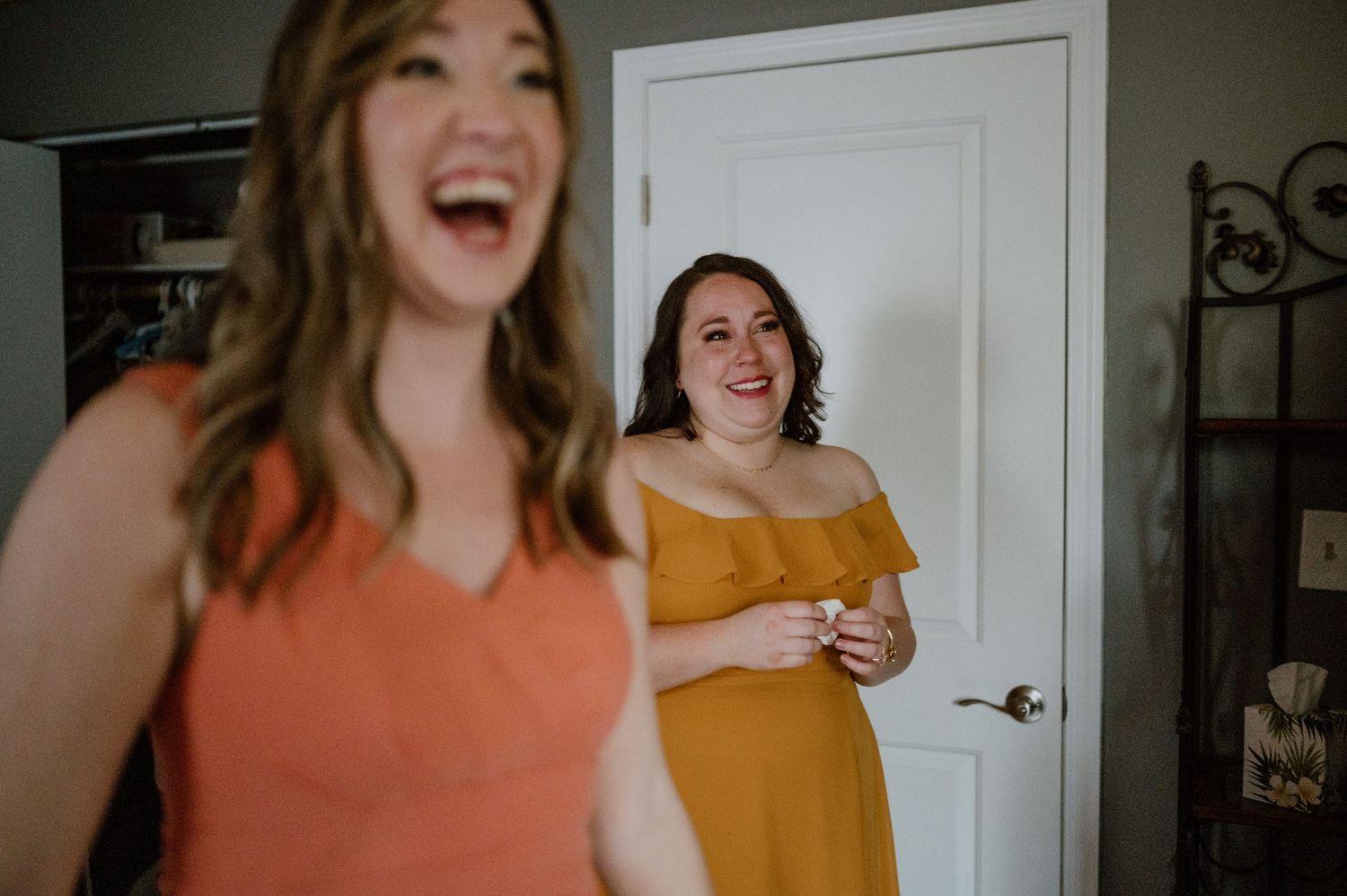 Joyful moment captured between friends in coral and mustard colored dresses.