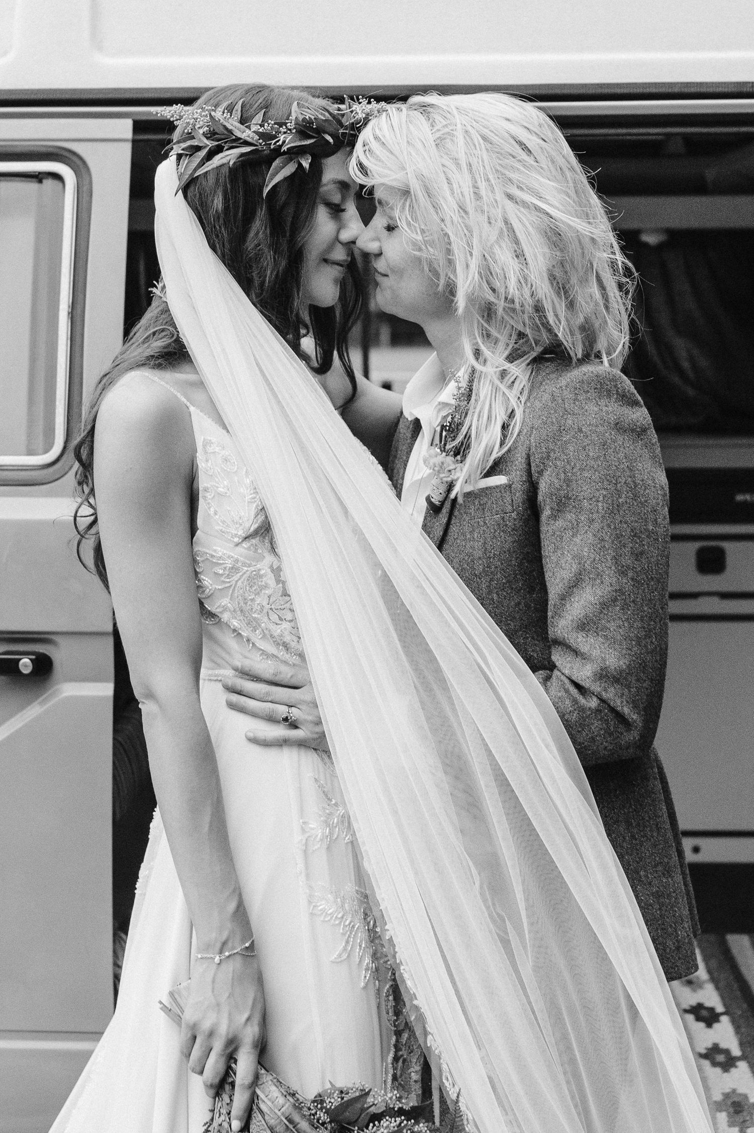 A romantic black and white portrait of newlyweds sharing a tender moment by a vintage van.