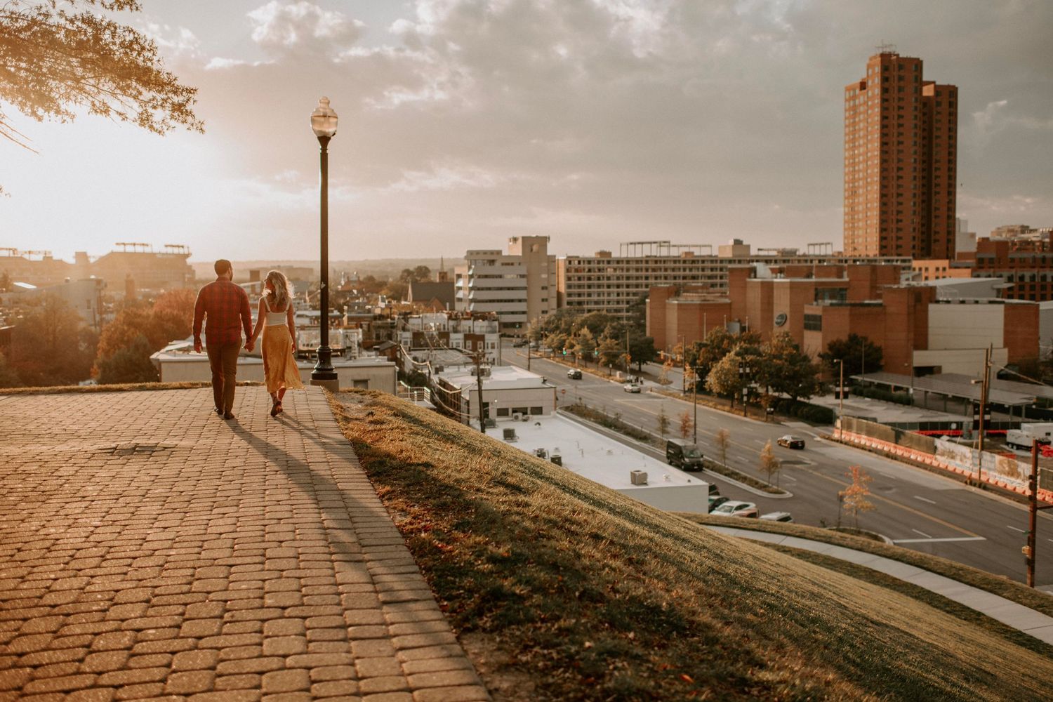 Silhouetted figures walking along brick path with dramatic city view at sunset.