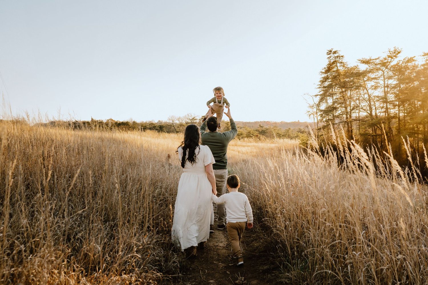 Family walking through golden grass field at sunset.