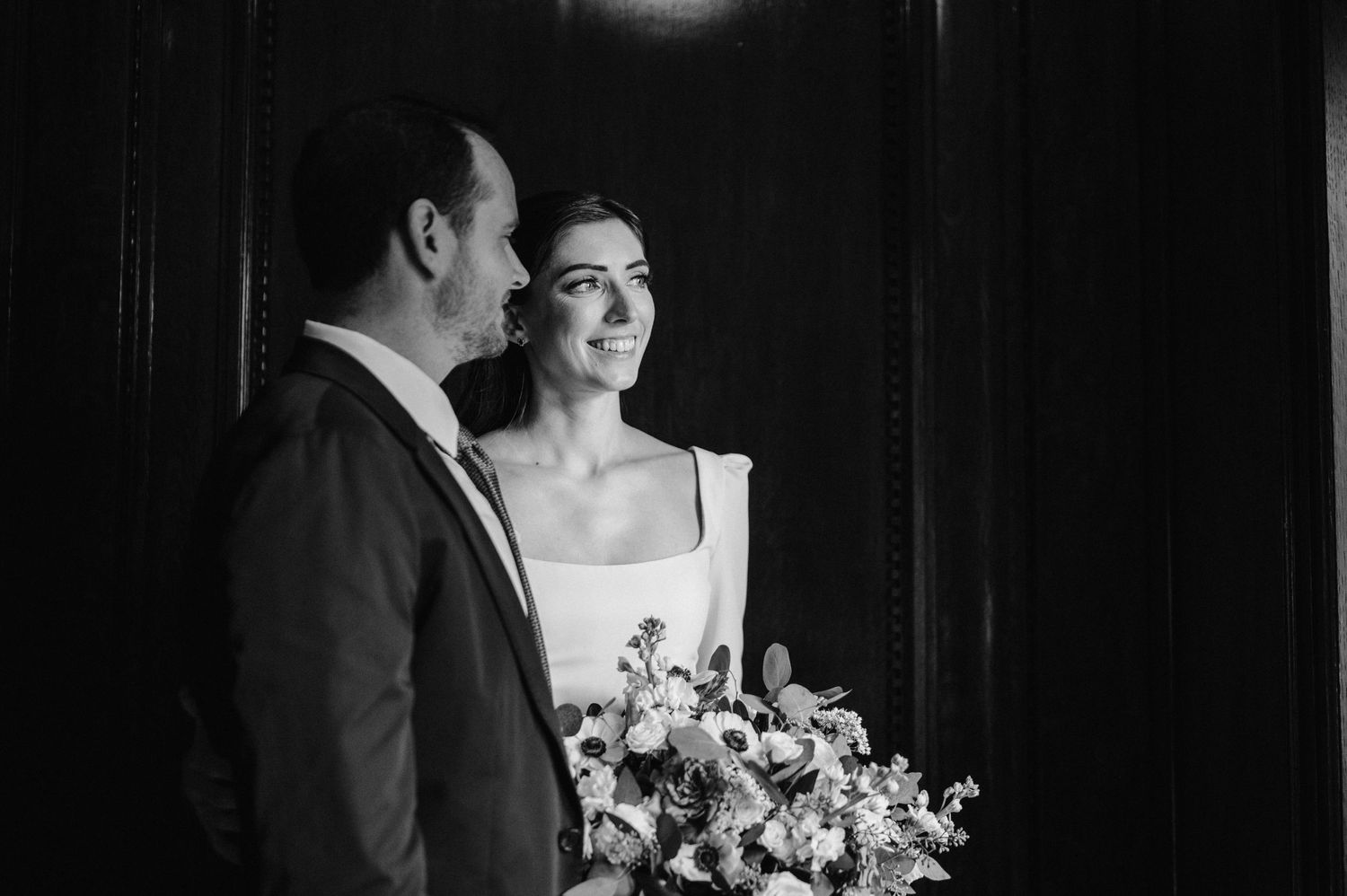 Romantic black and white portrait with floral bouquet against dark background.