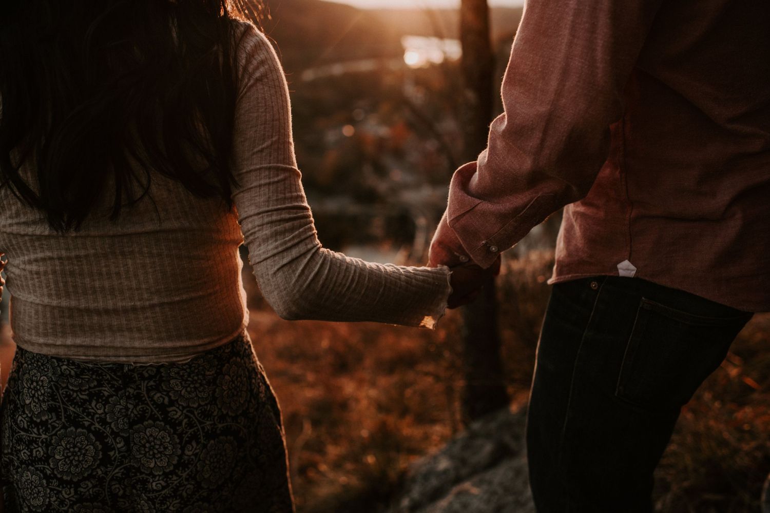 Close up of couple holding hands against autumn sunset backdrop.