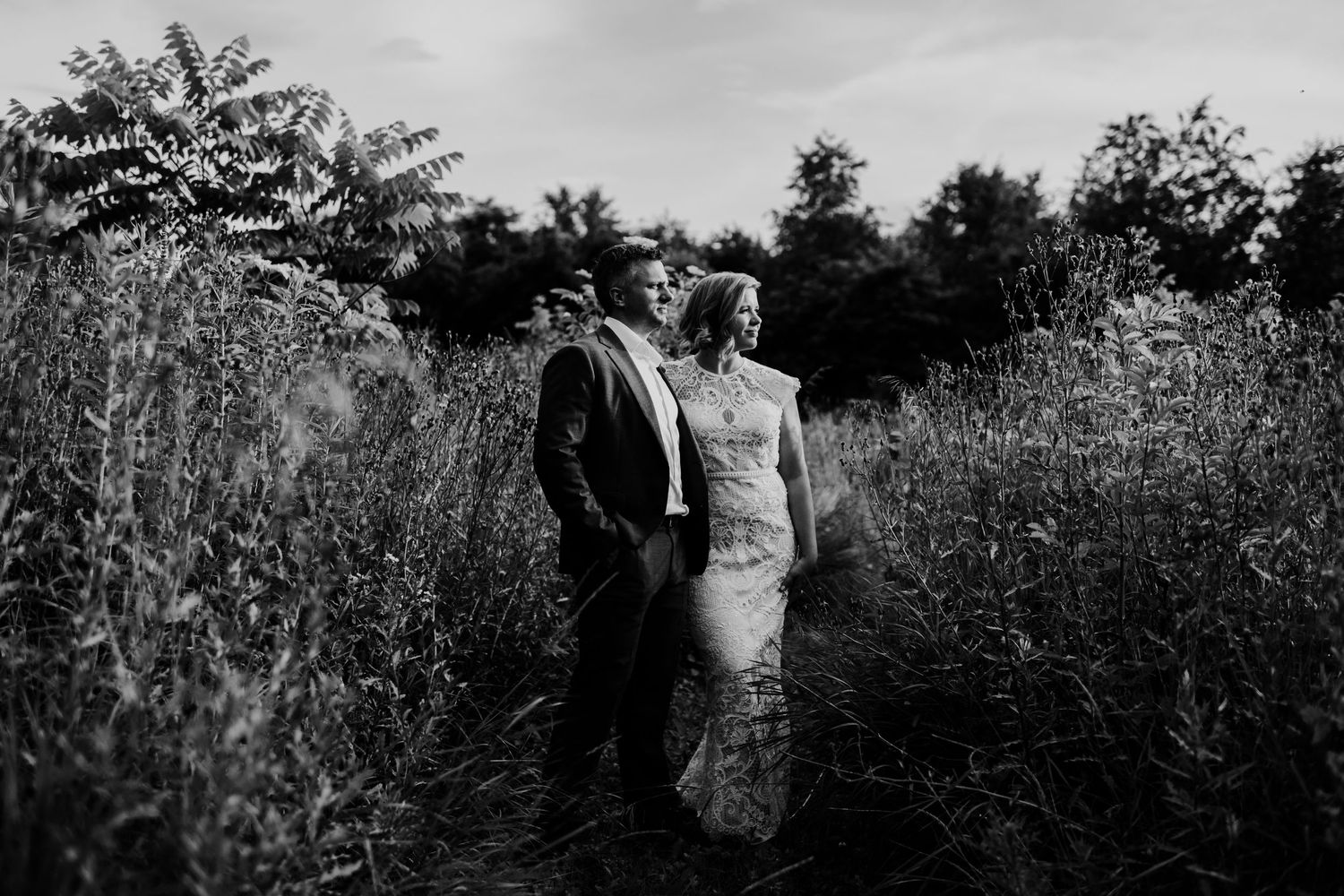 A couple poses together in a field of tall grass and wildflowers at golden hour.