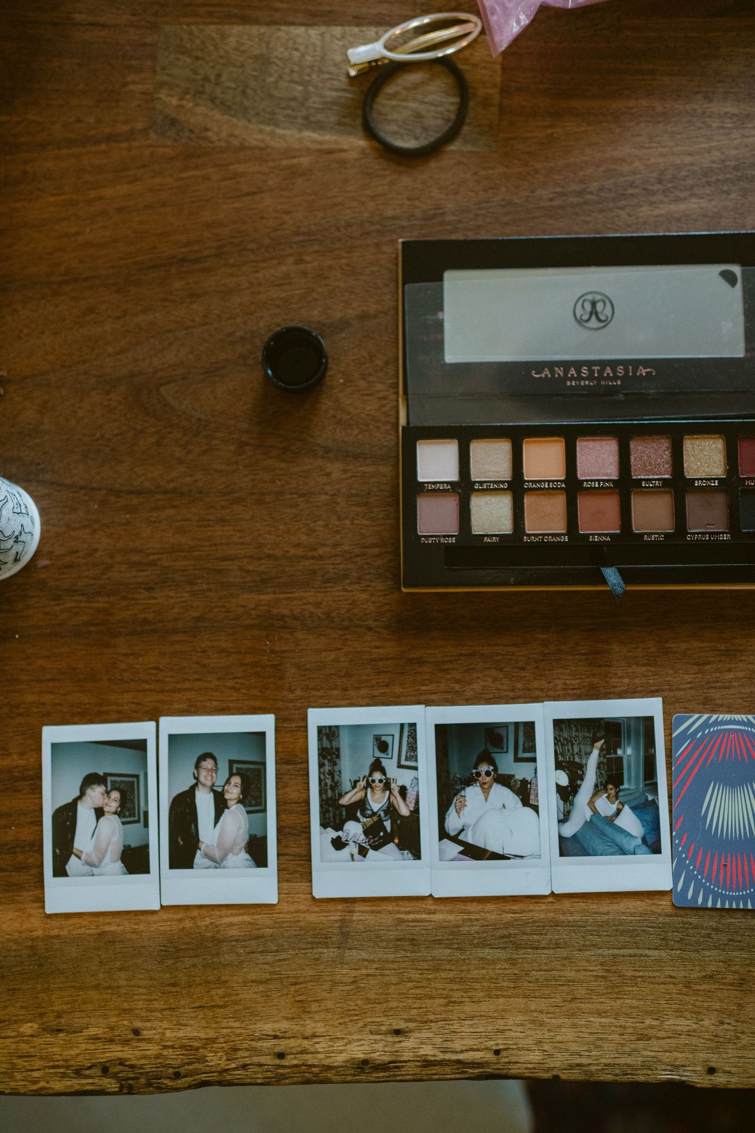 Makeup palette and vintage polaroid photos arranged on wooden table surface.