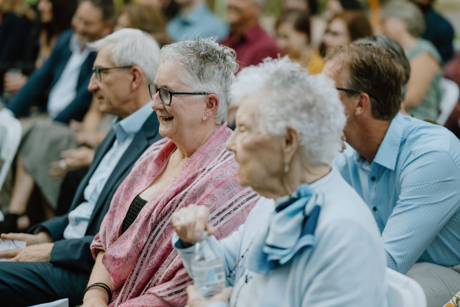 Wedding guests of various ages seated in rows during an outdoor ceremony.