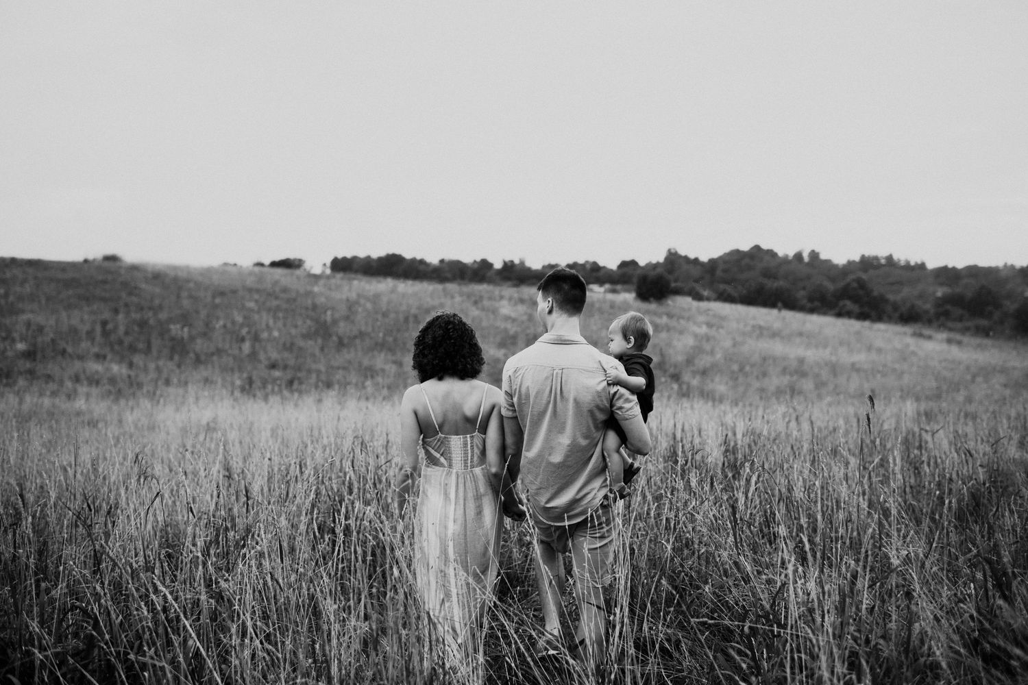 Intimate black and white portrait of parent embracing baby in outdoor field setting.