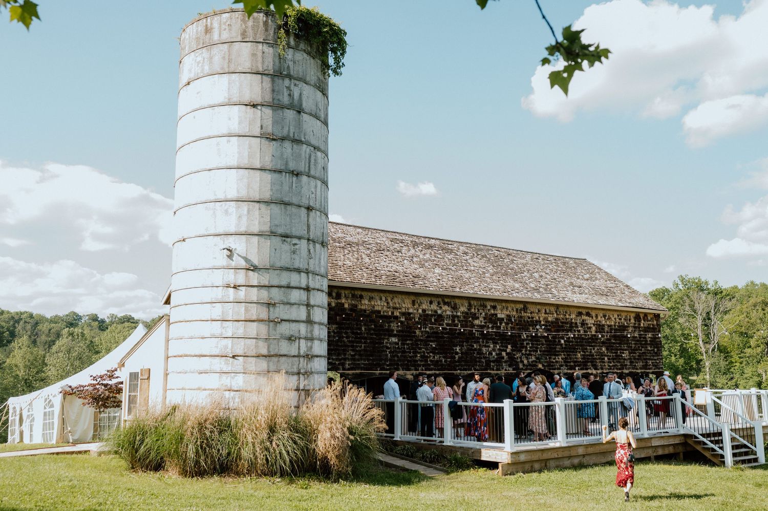 A rustic barn wedding venue with a large white silo and guests gathering outside.
