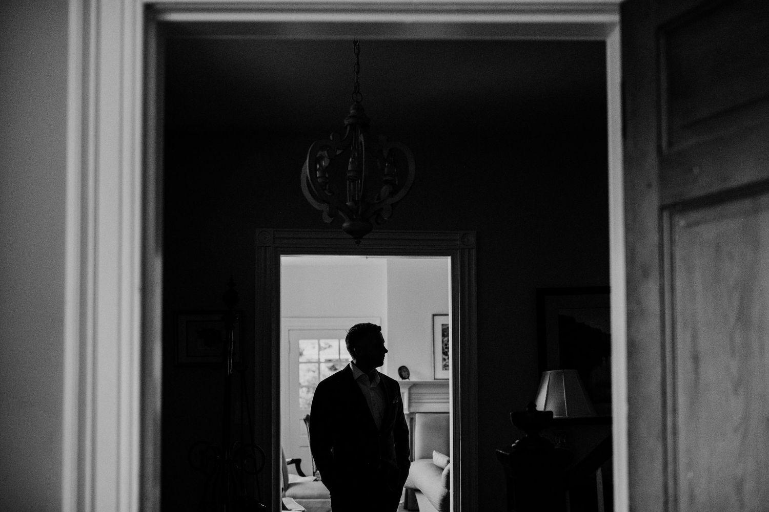 Silhouette of person standing in dark doorway with chandelier above.
