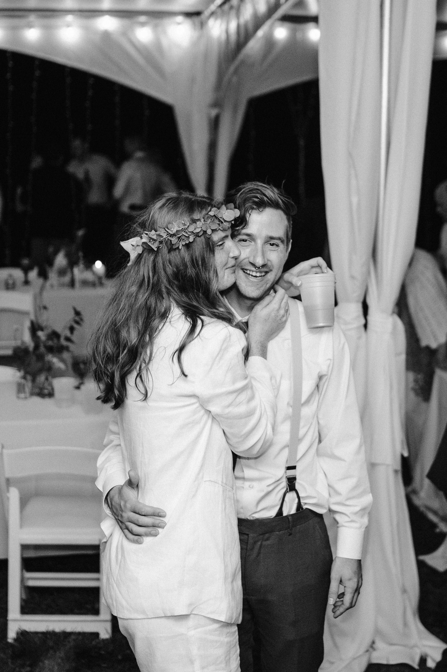 A couple shares an intimate moment under a white tent at their wedding reception.