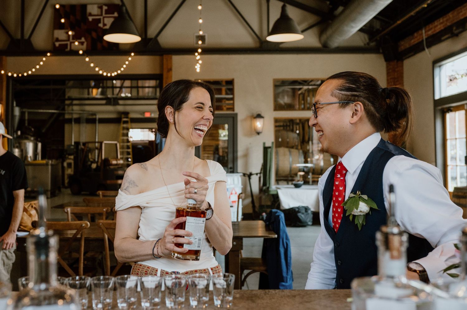 Celebratory drinks being shared in a rustic distillery setting with string lights.
