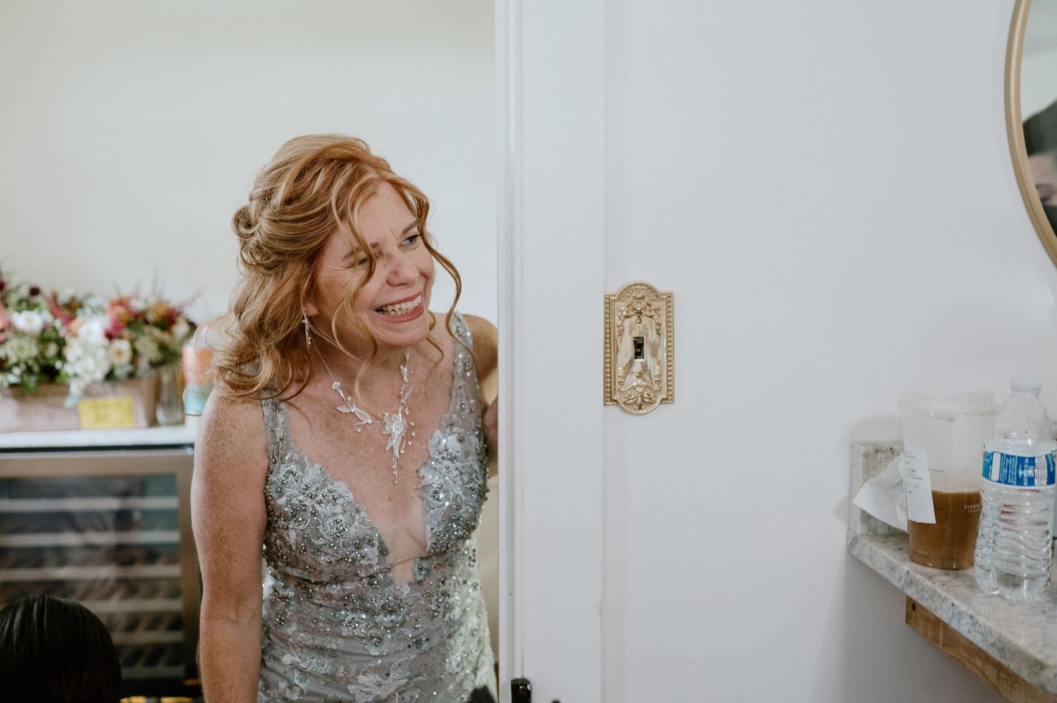 Someone in a sparkly silver evening gown smiling joyfully in a white room.
