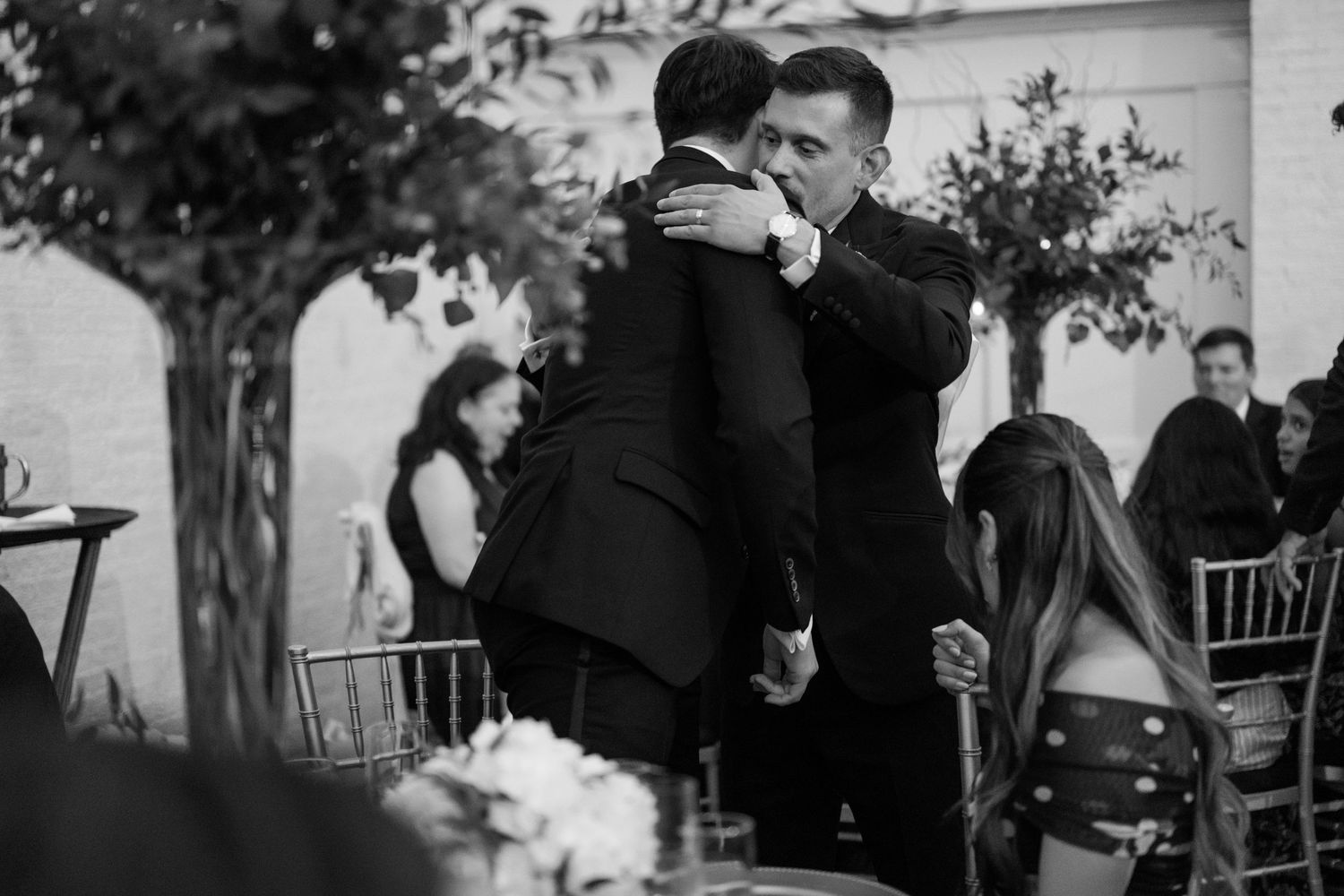 Wedding guests gathered outdoors for a casual celebration under trees on a sunny day.