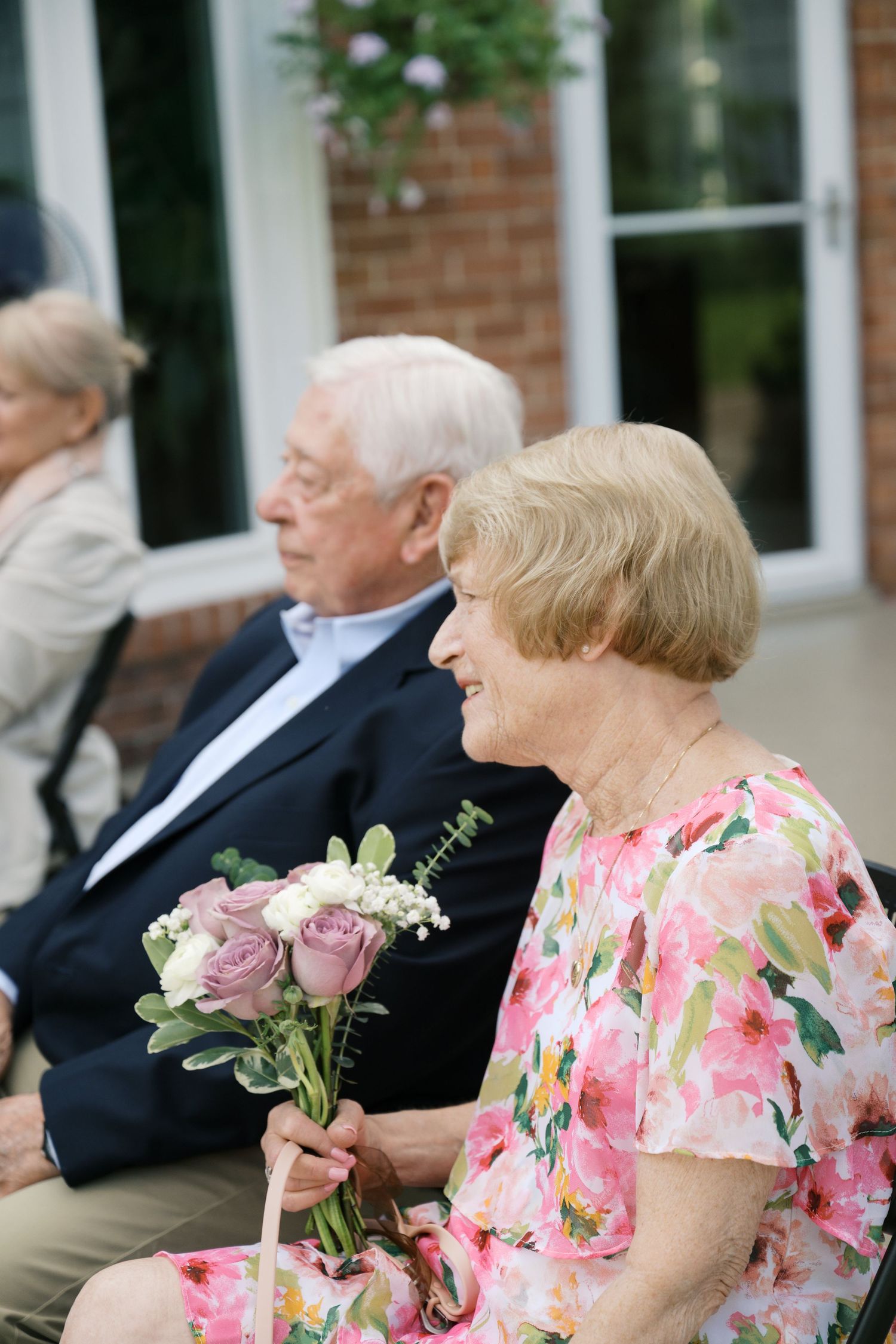 Wedding guests in formal attire seated outdoors with pink floral decorations and roses.