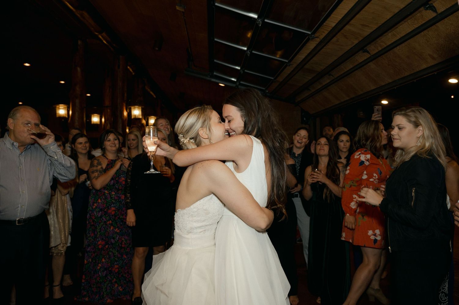 Wedding reception guests dance and celebrate in an intimate indoor venue with soft lighting.