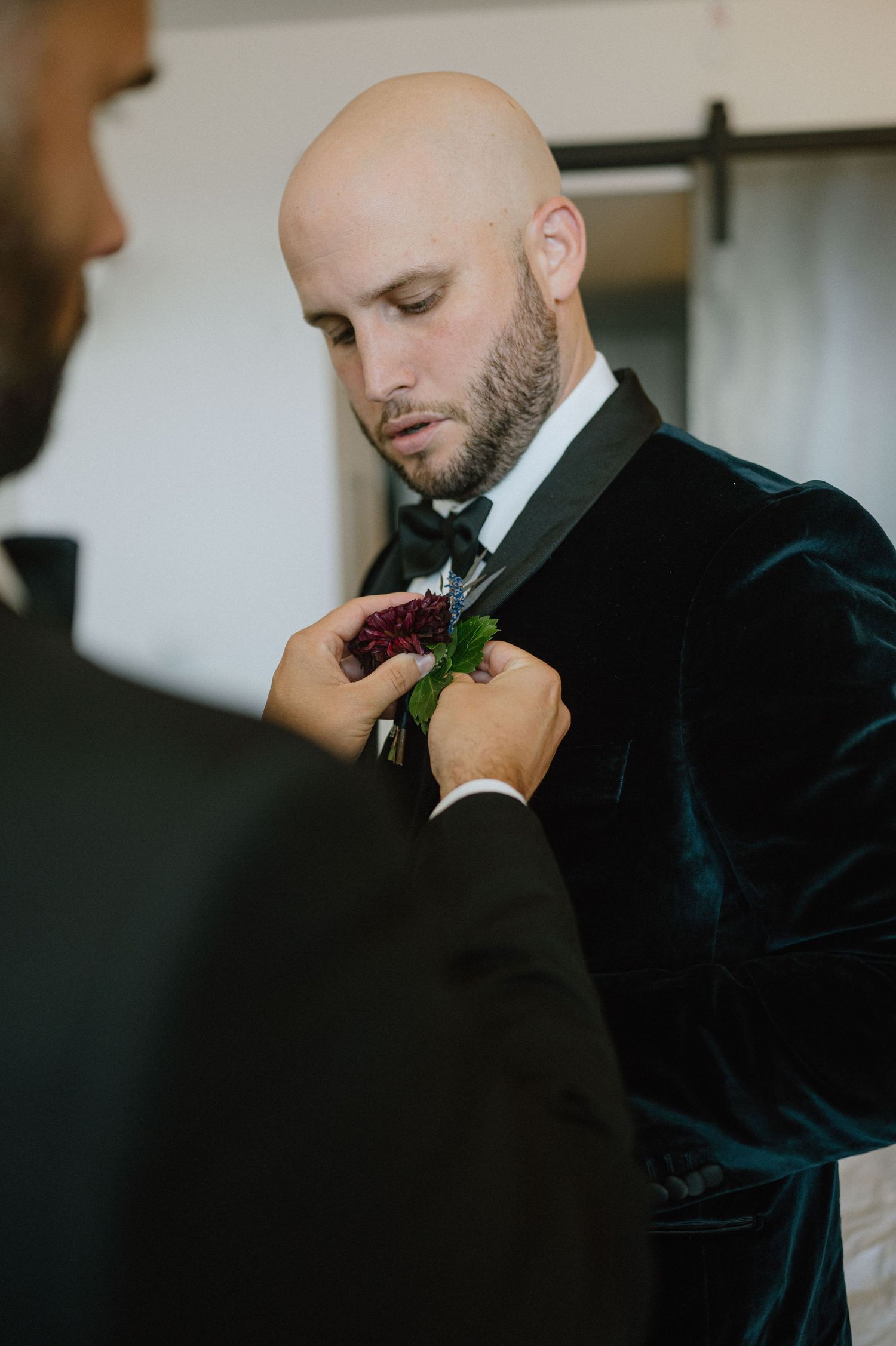 A boutonniere being pinned on a dark velvet suit jacket during wedding preparations.