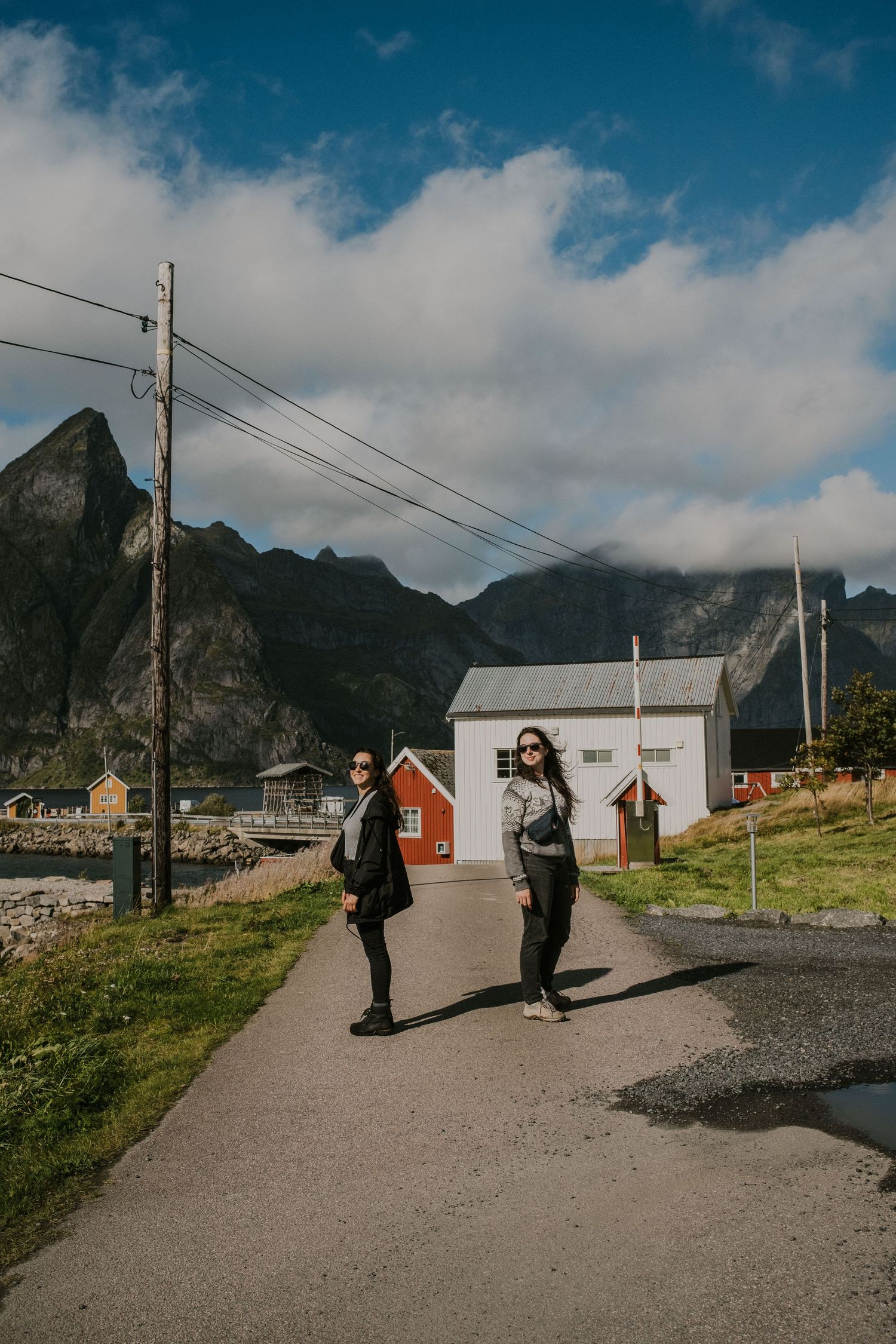 People walking on path through coastal village with dramatic mountain backdrop in Norway.