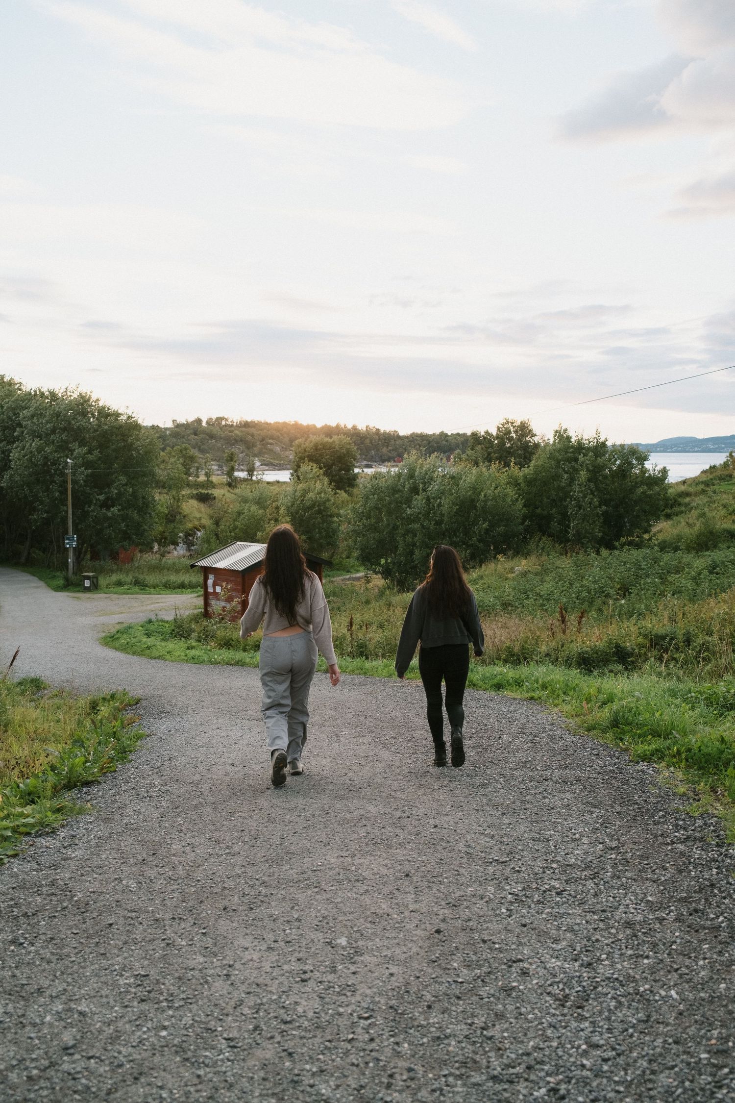 Two people walking down a gravel path surrounded by green landscape at sunset.