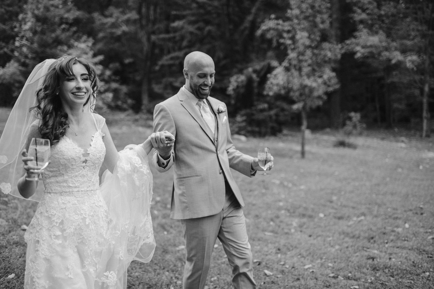 Black and white candid photo of newlyweds laughing and walking together outdoors.