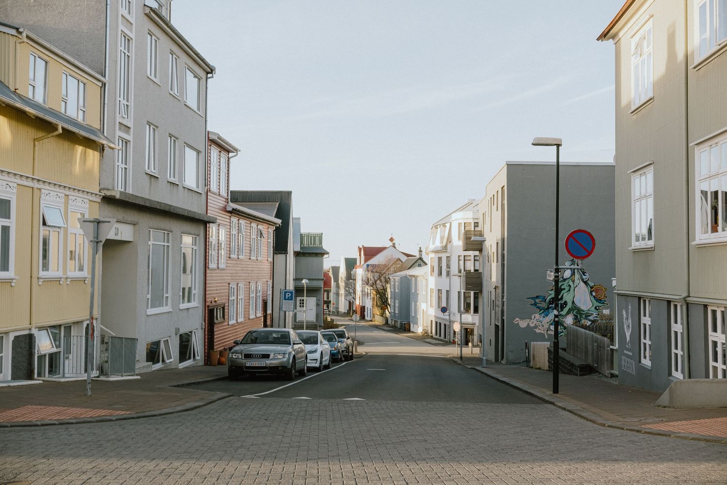 Quiet residential street with parked cars between modern buildings in an urban setting.