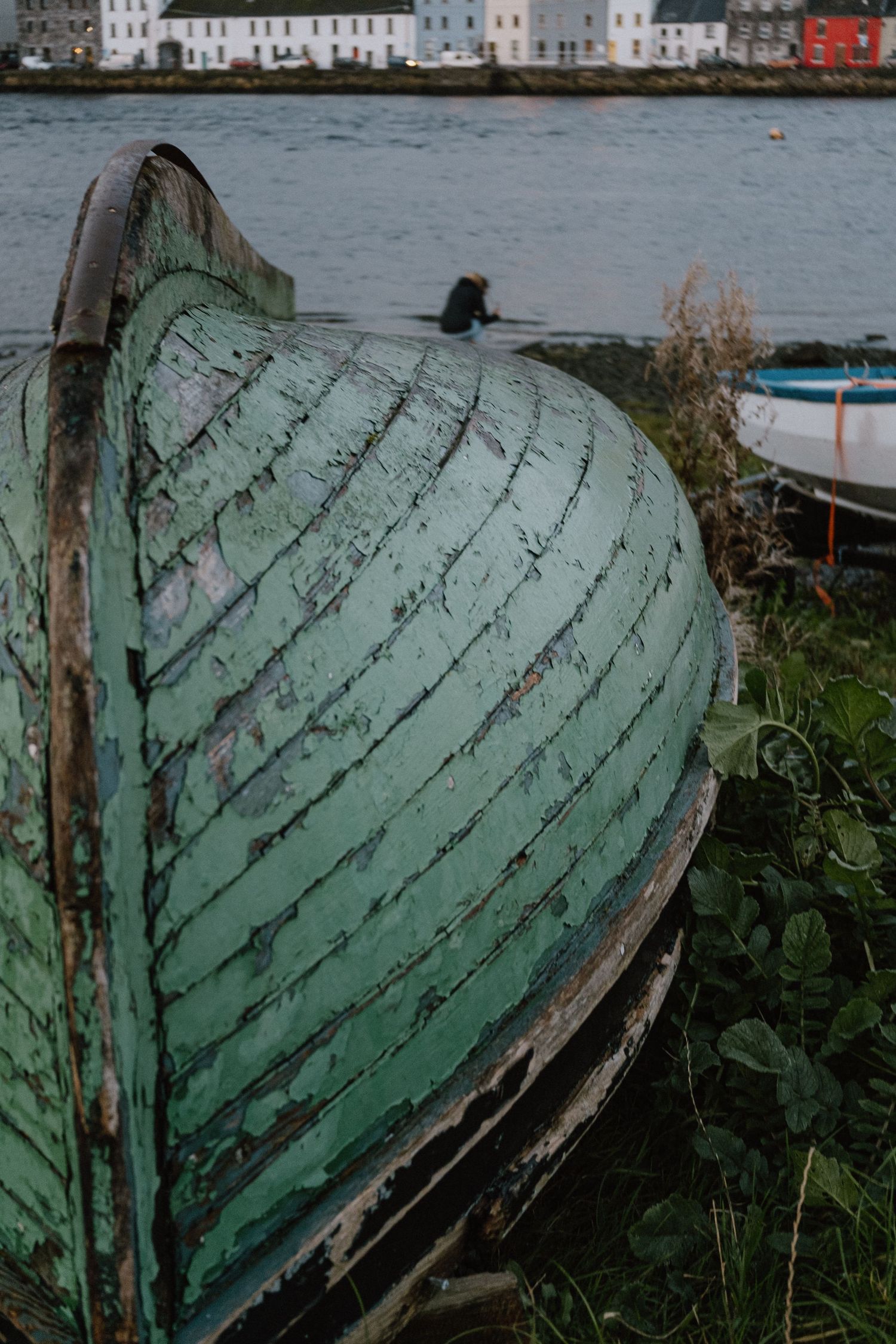 An old weathered green boat hull lies abandoned on the shoreline.