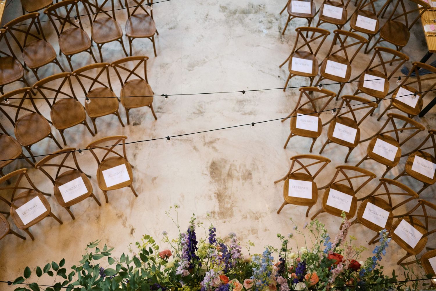 Wooden cross-back chairs arranged in curved rows with floral aisle decorations.