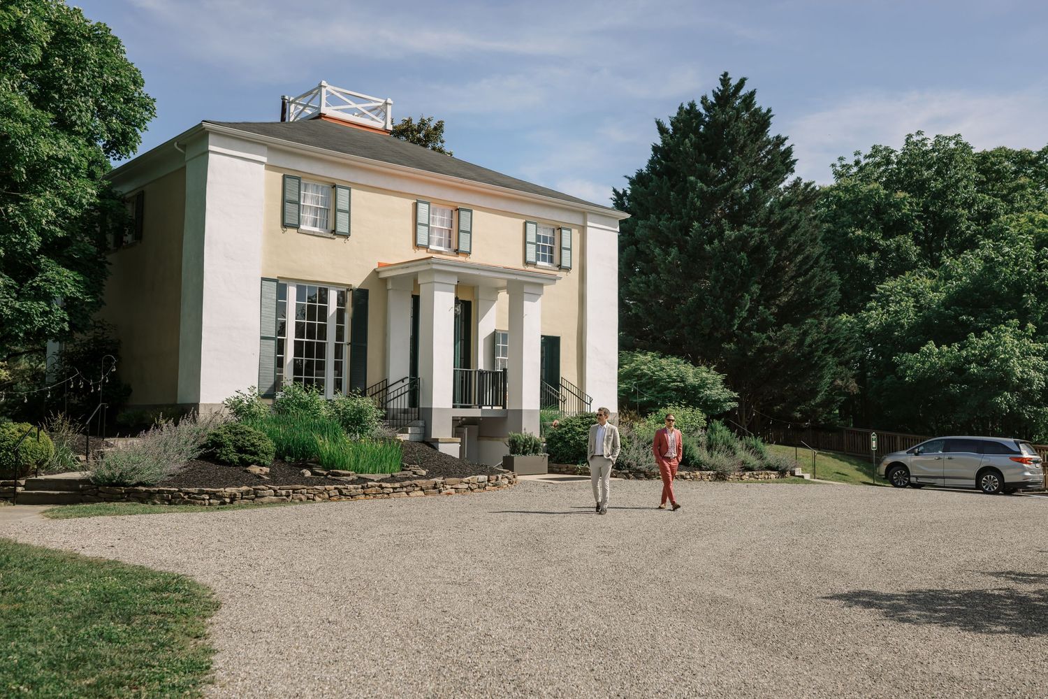 Elegant white colonial-style house with pillars and gravel driveway.