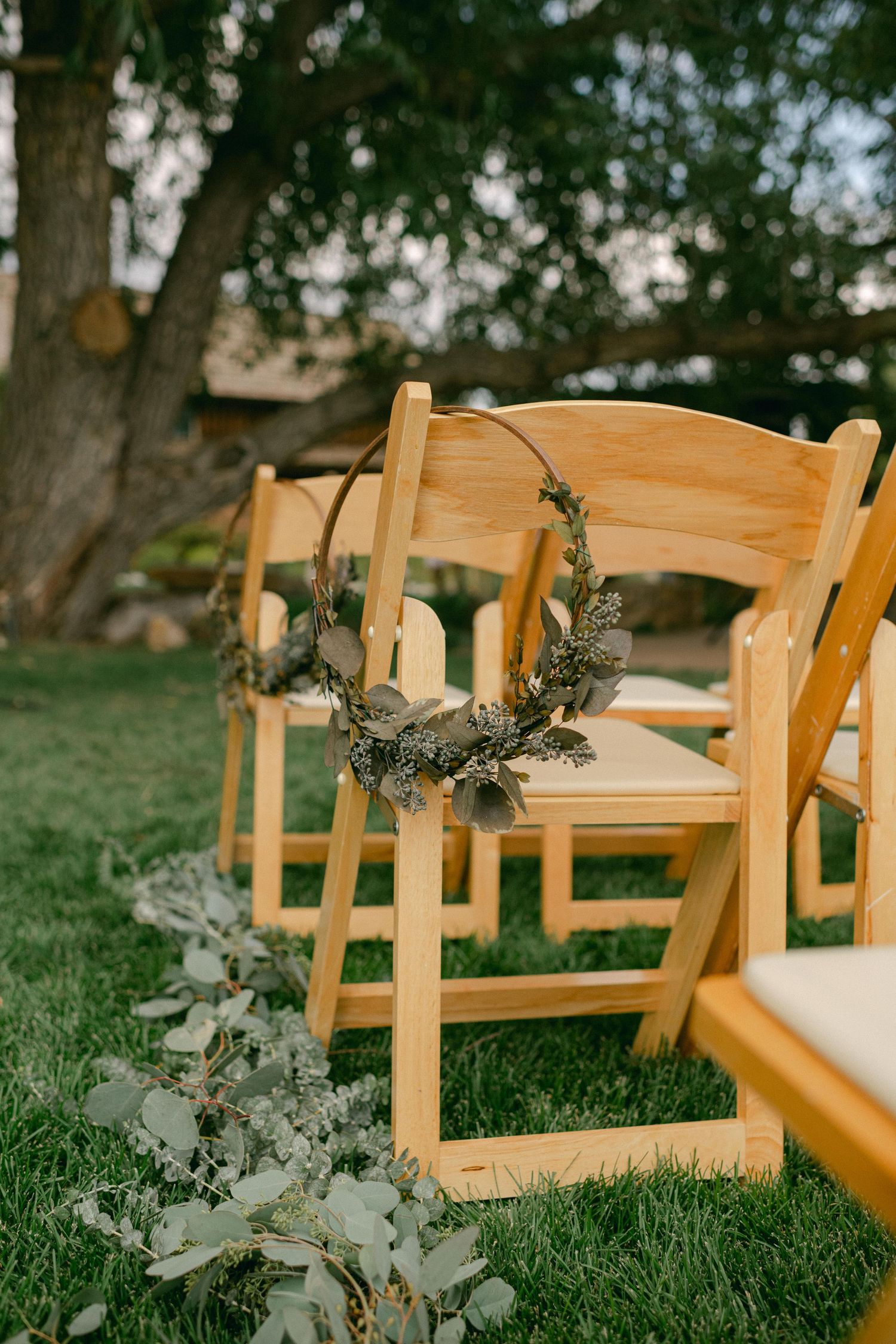 Wooden folding chairs decorated with floral wreaths arranged on grass for an outdoor wedding ceremony.