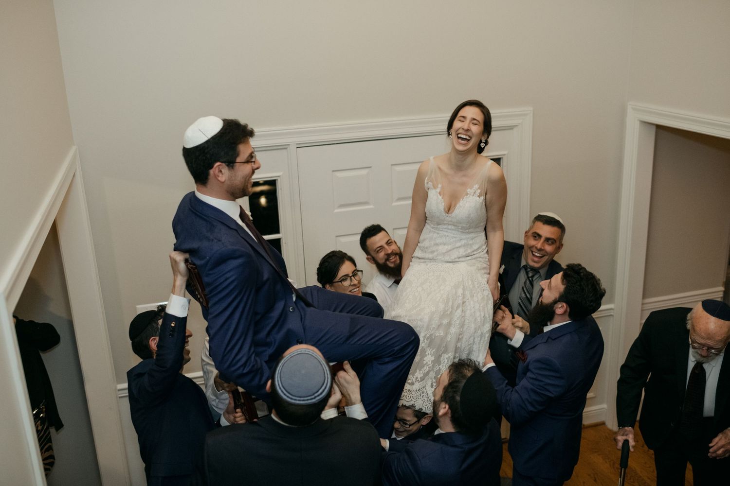 Traditional Jewish wedding hora dance celebration with guests lifting couple in chairs.