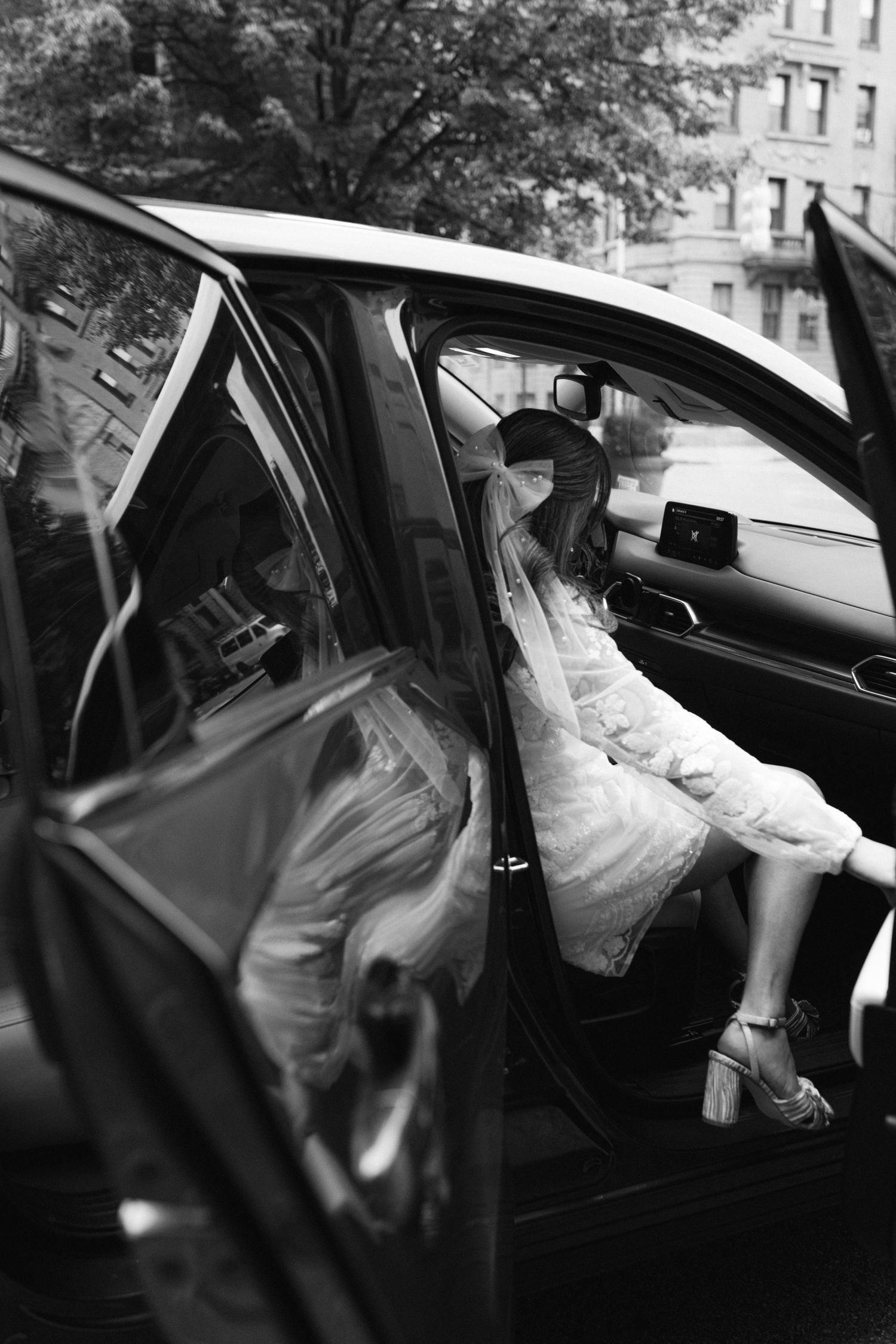 A person in white clothing entering a black car on a city street.
