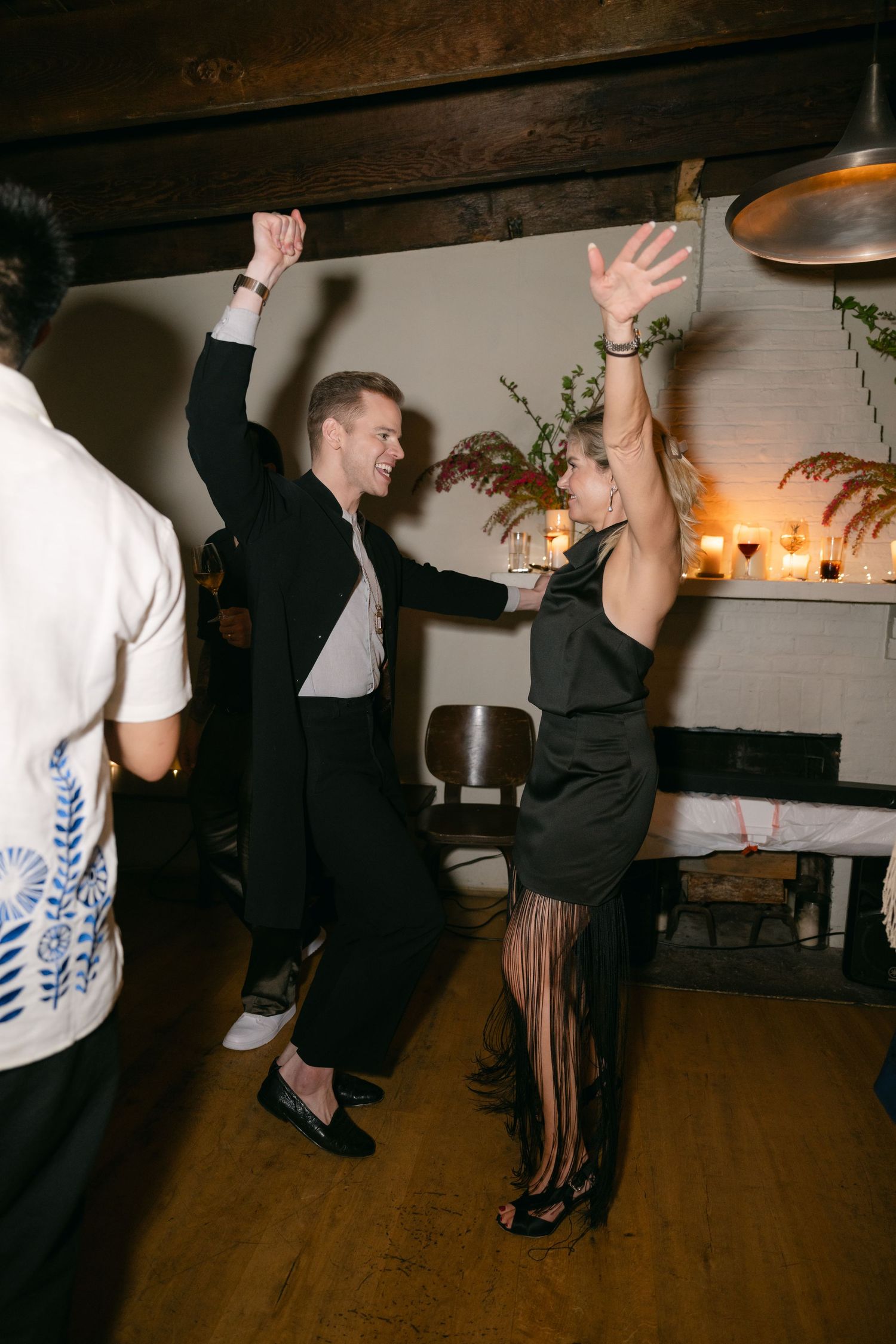 Elegantly dressed couple energetically dancing together at an indoor celebration with ambient lighting and wooden beams.