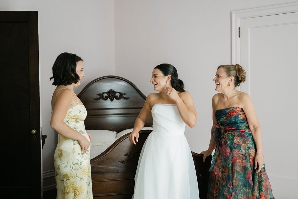 Wedding dress preparation scene with bridesmaids in floral dresses helping with final adjustments.