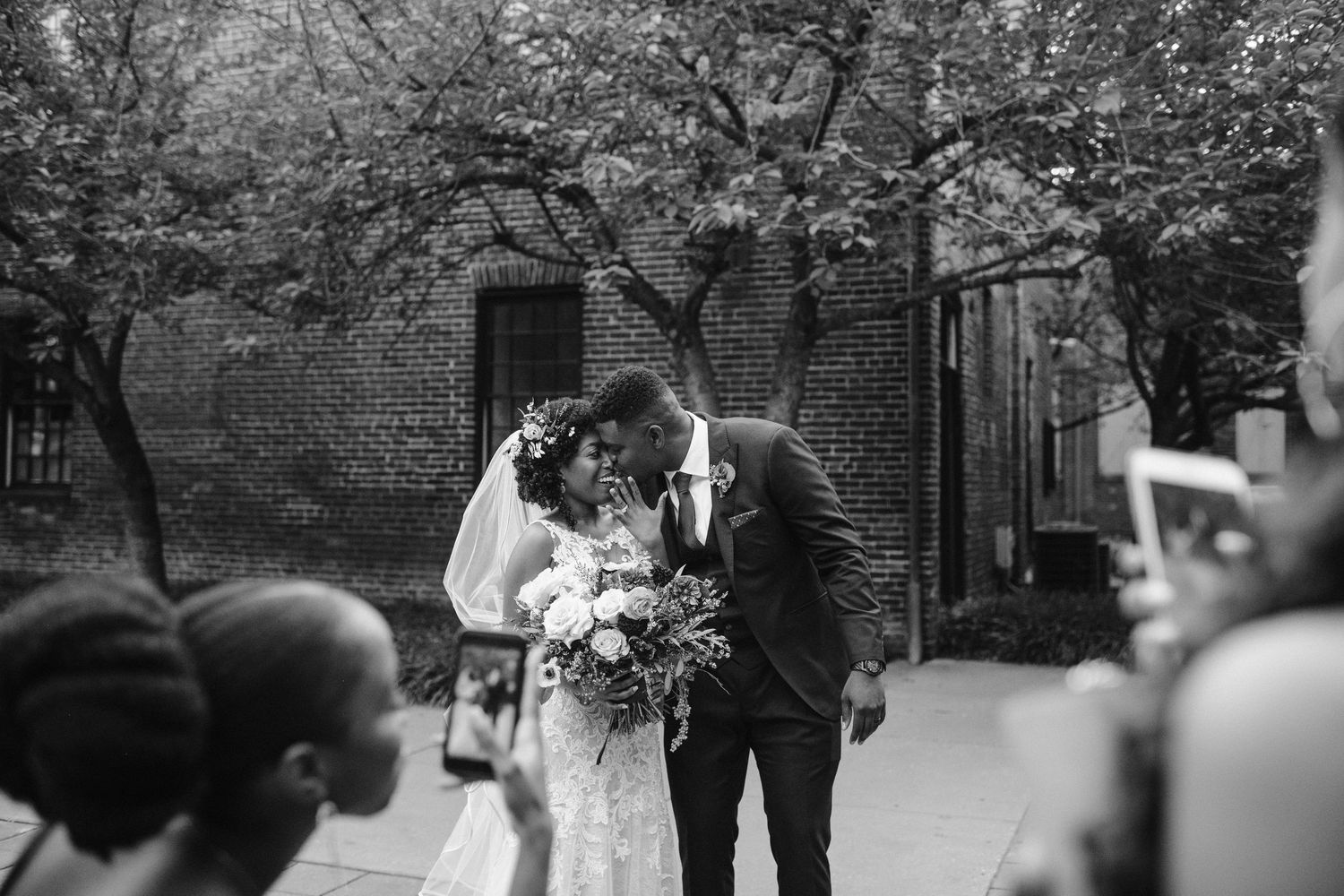 A wedding ceremony in progress with guests gathered outdoors under trees.