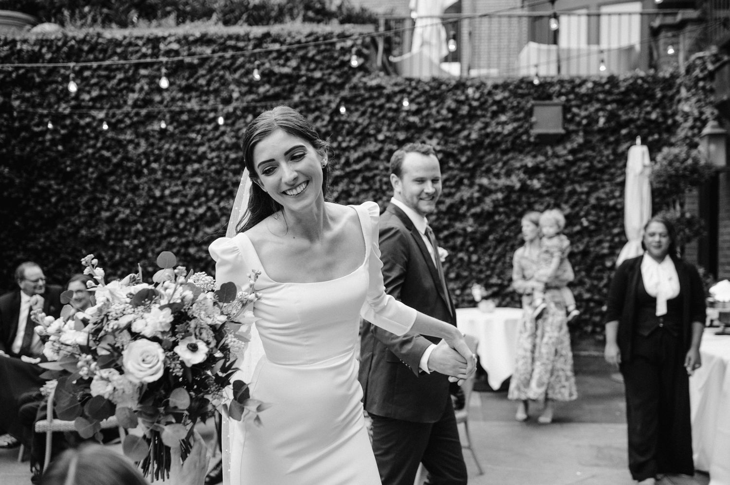 Joyful celebration moment at an outdoor wedding reception with greenery backdrop.