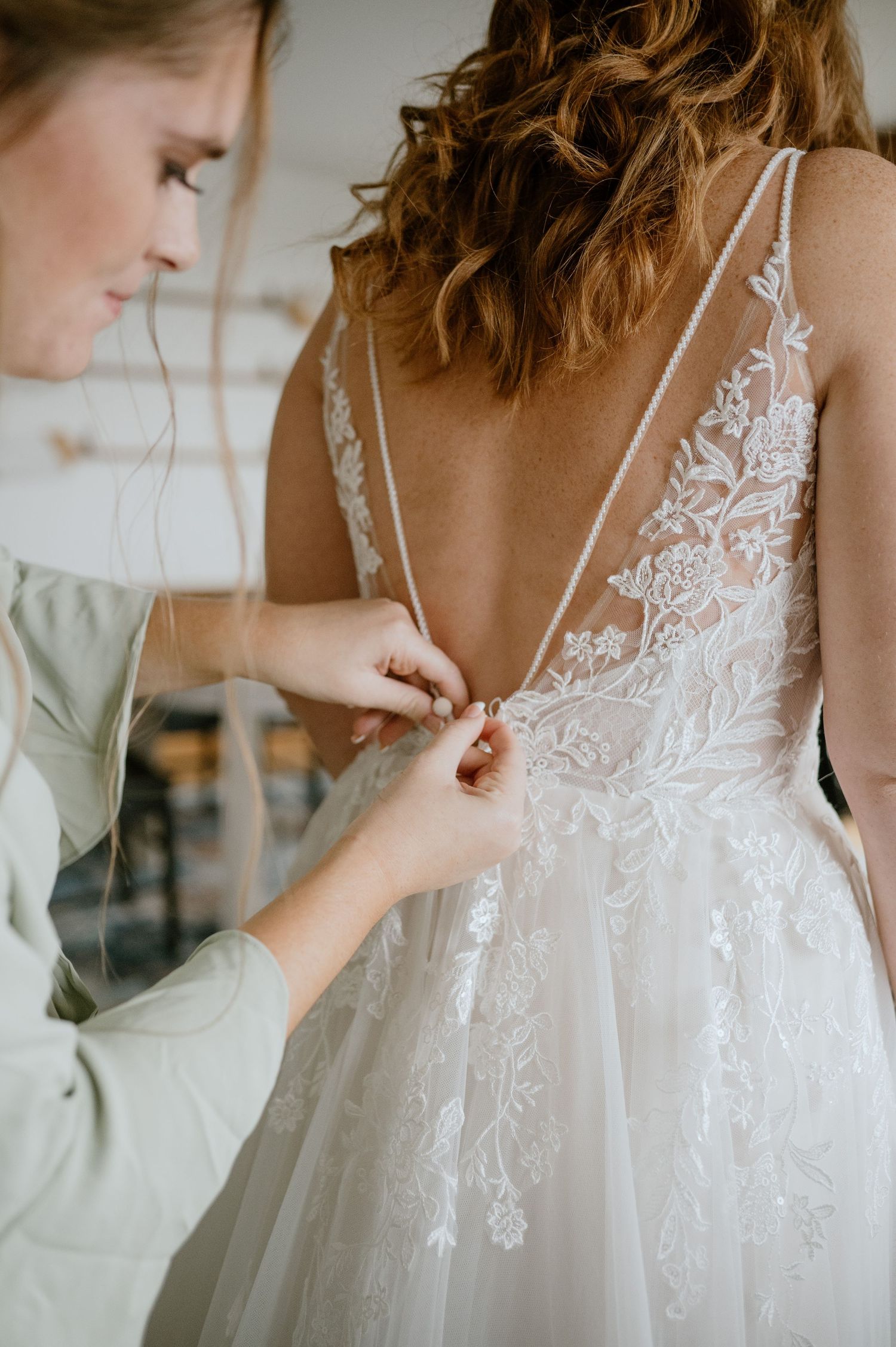 Close-up of intricate lace detail on back of white wedding dress being fastened.