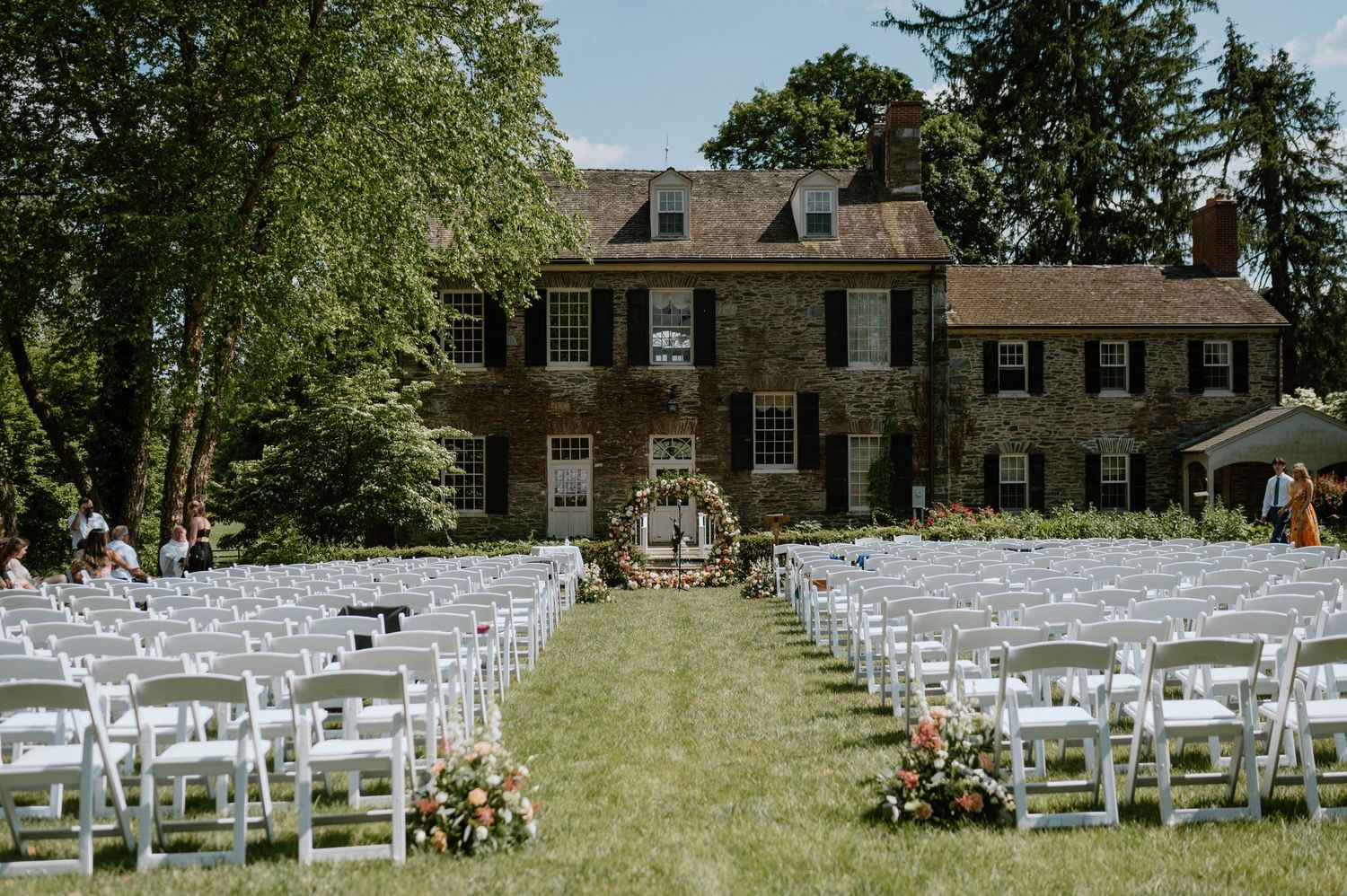 White chairs lined up on a lawn for an outdoor wedding ceremony in front of a historic mansion.