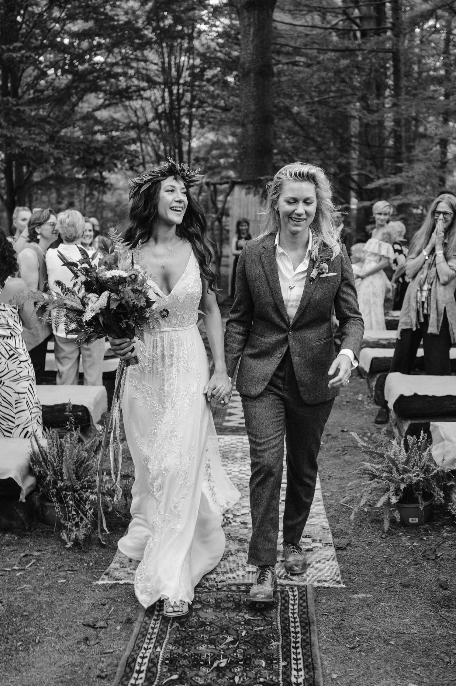 A happy couple walks down the forest aisle after their wedding ceremony in black and white.