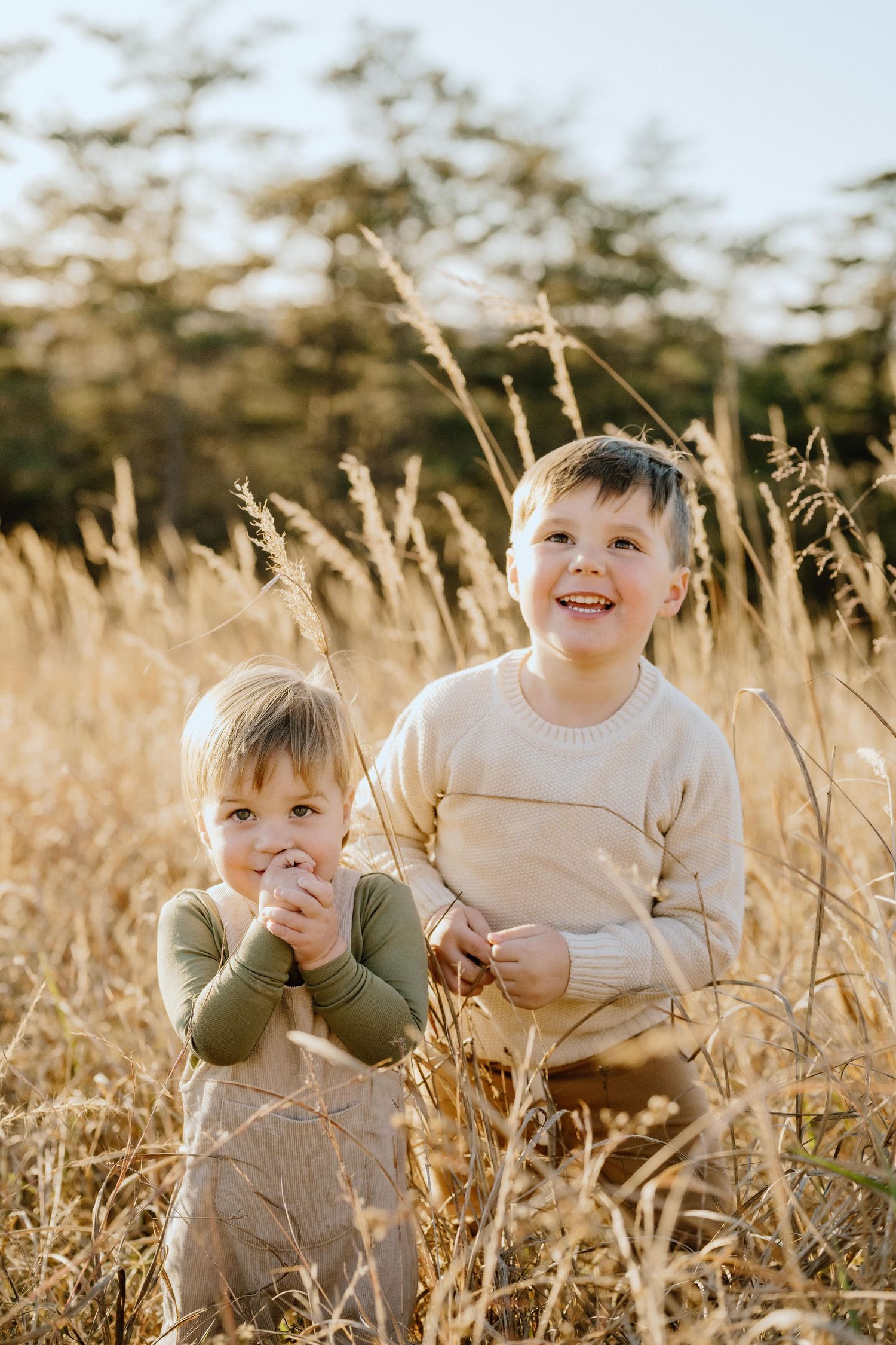Two children smiling and playing together in a field of tall wheat at golden hour.