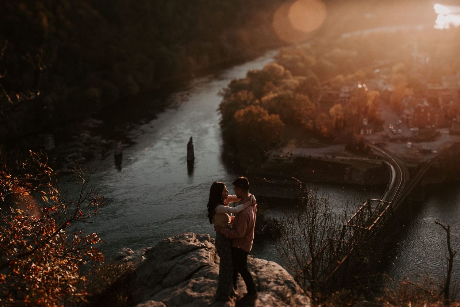 Couple shares intimate moment on clifftop overlooking winding river at sunset.