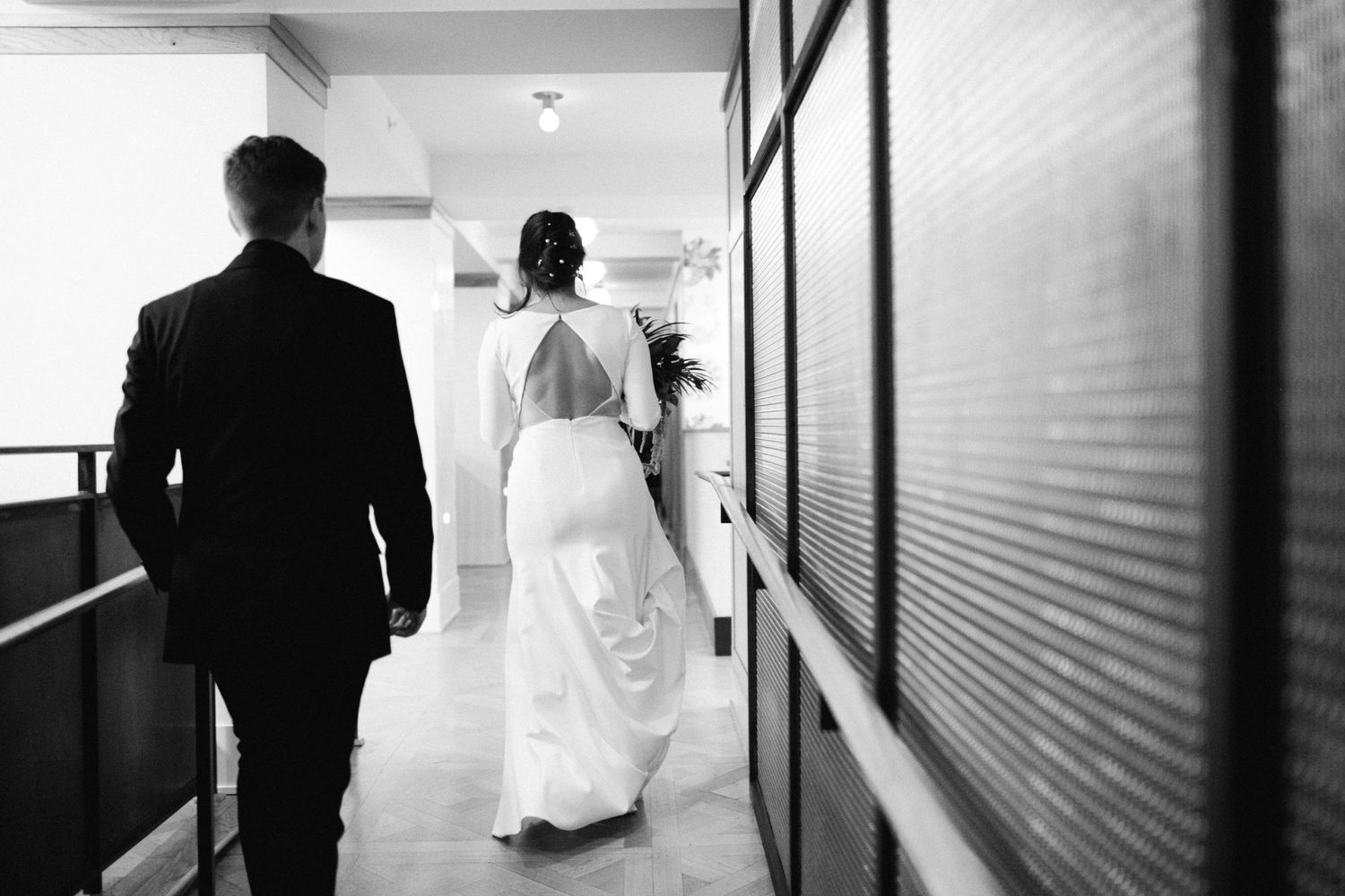Black and white photo of wedding couple walking down modern hallway.