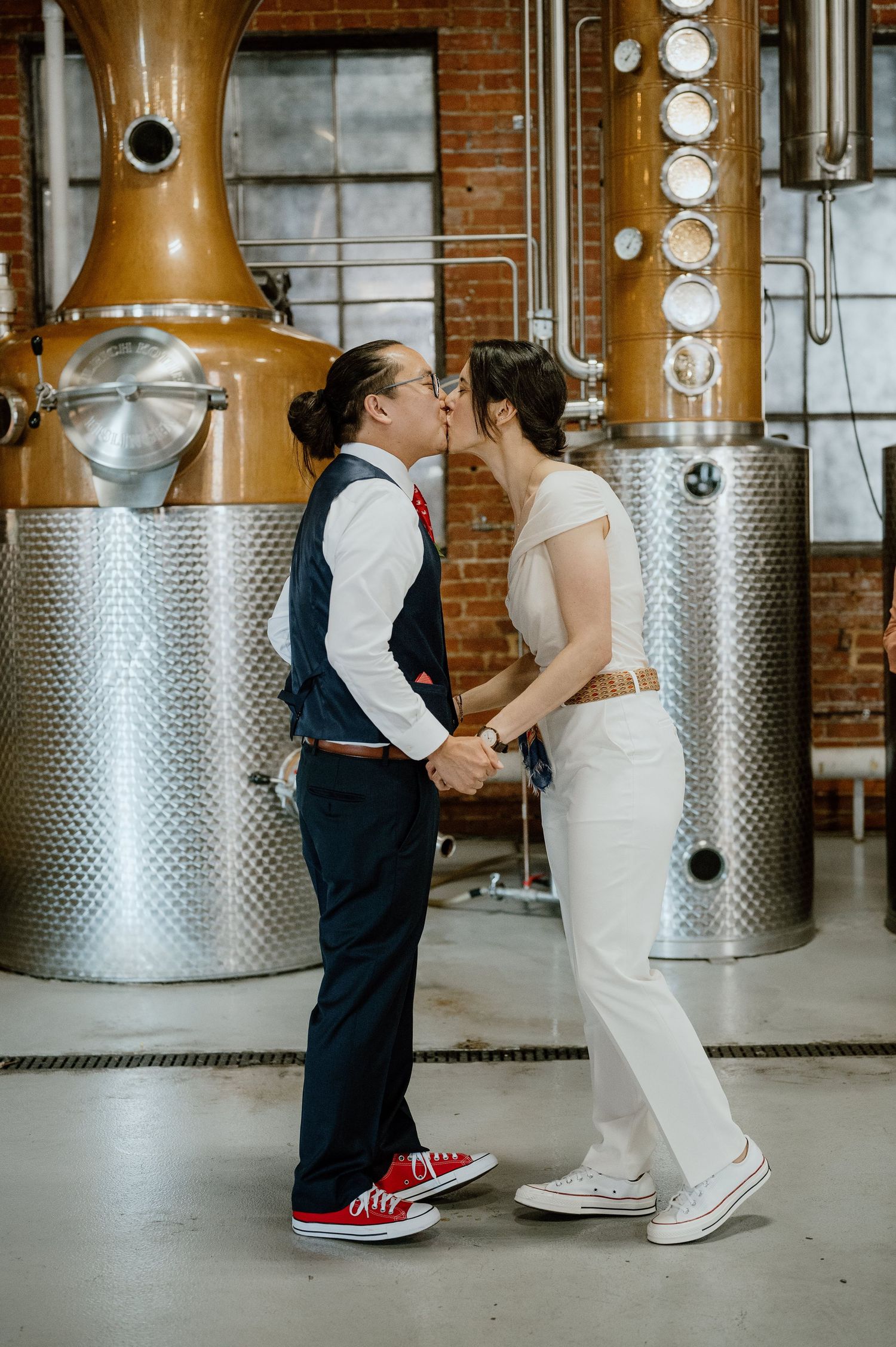 A couple sharing an intimate moment in front of copper distillery equipment.