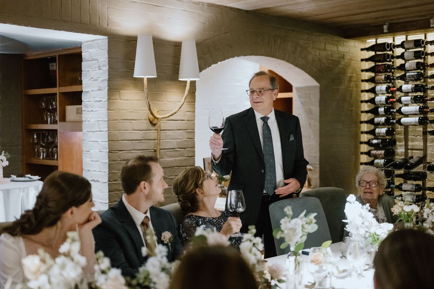 A wedding toast being delivered in an intimate restaurant setting with elegant decor.
