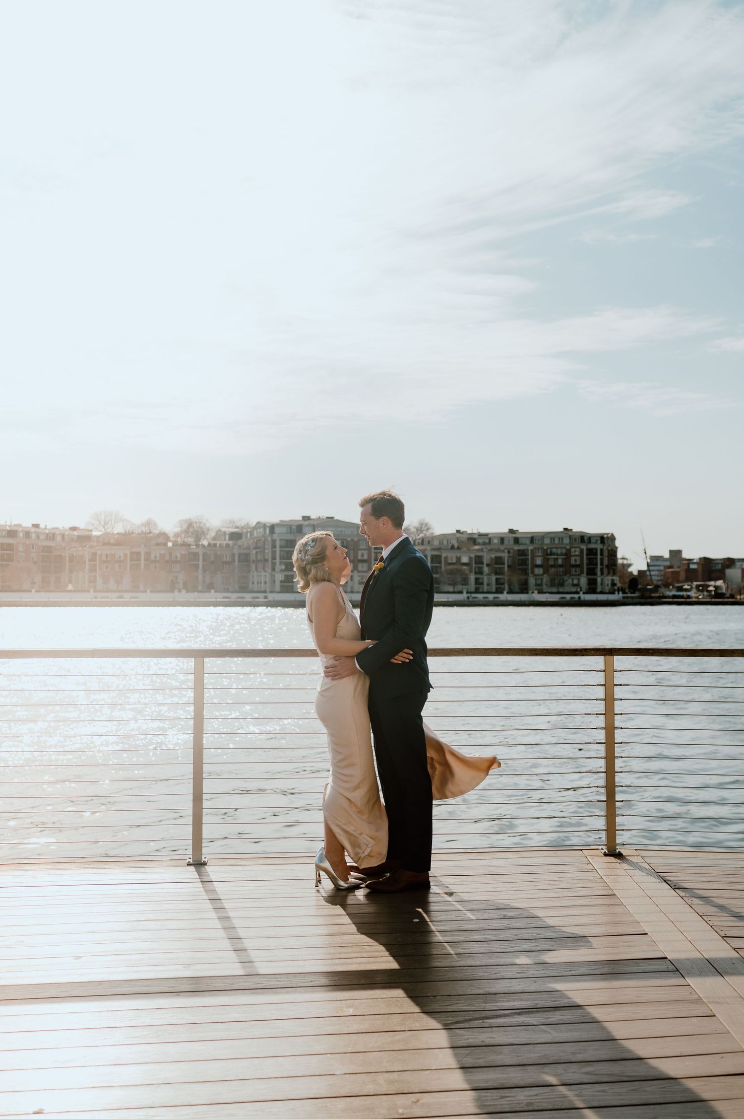 Sun-drenched wedding portrait of couple standing on waterfront deck.