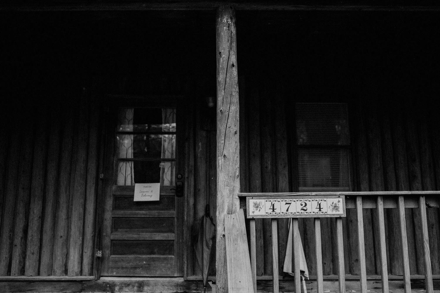 Black and white image of a rustic cabin porch with vintage architectural details.