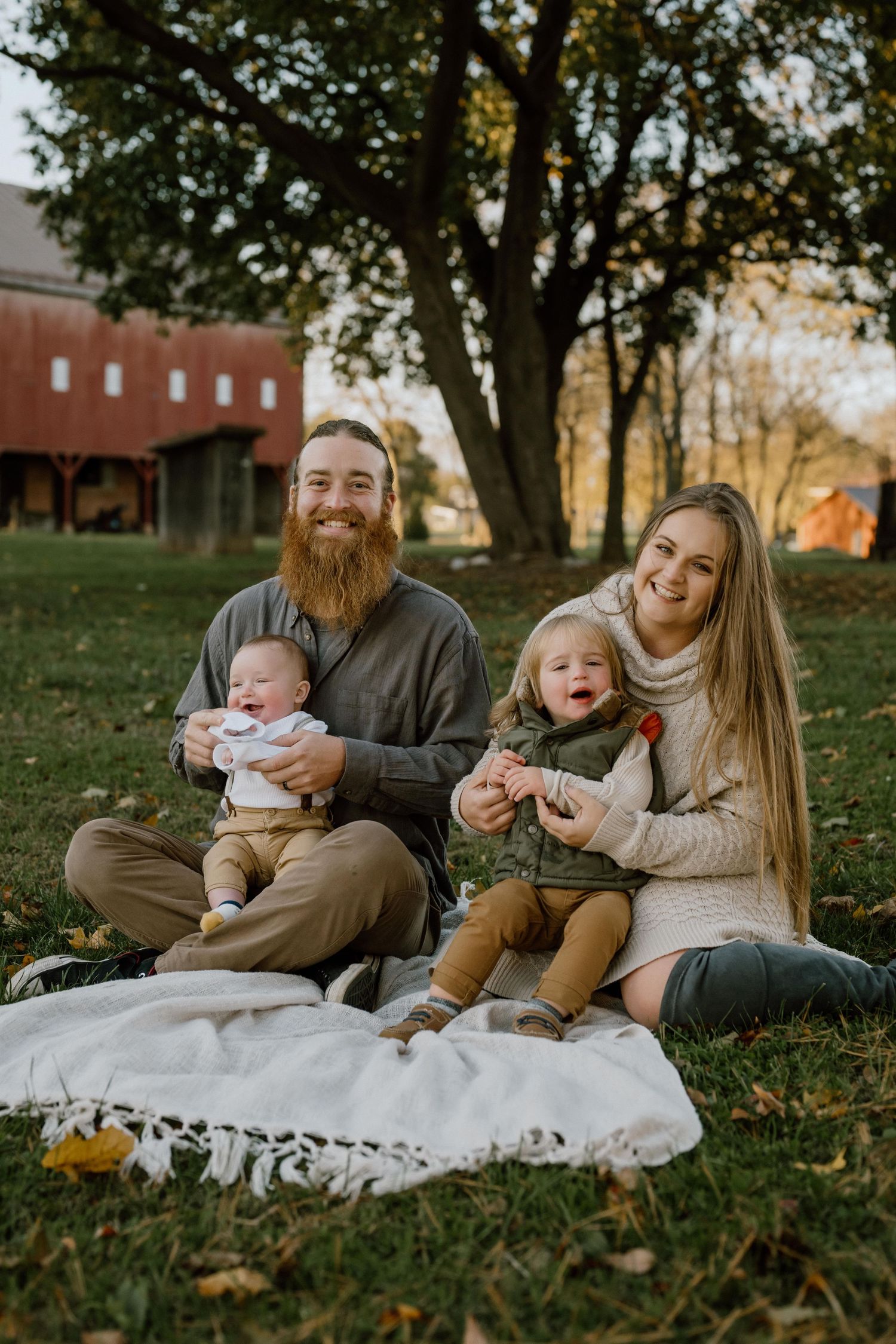 A family sits together on a white blanket during an autumn photo session.
