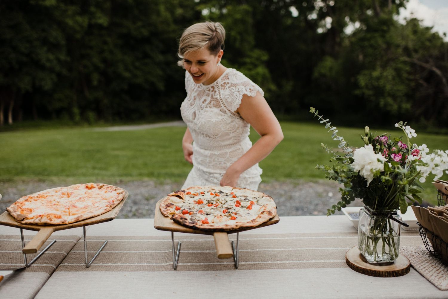 Wedding reception featuring fresh pizzas and floral arrangements on outdoor table.