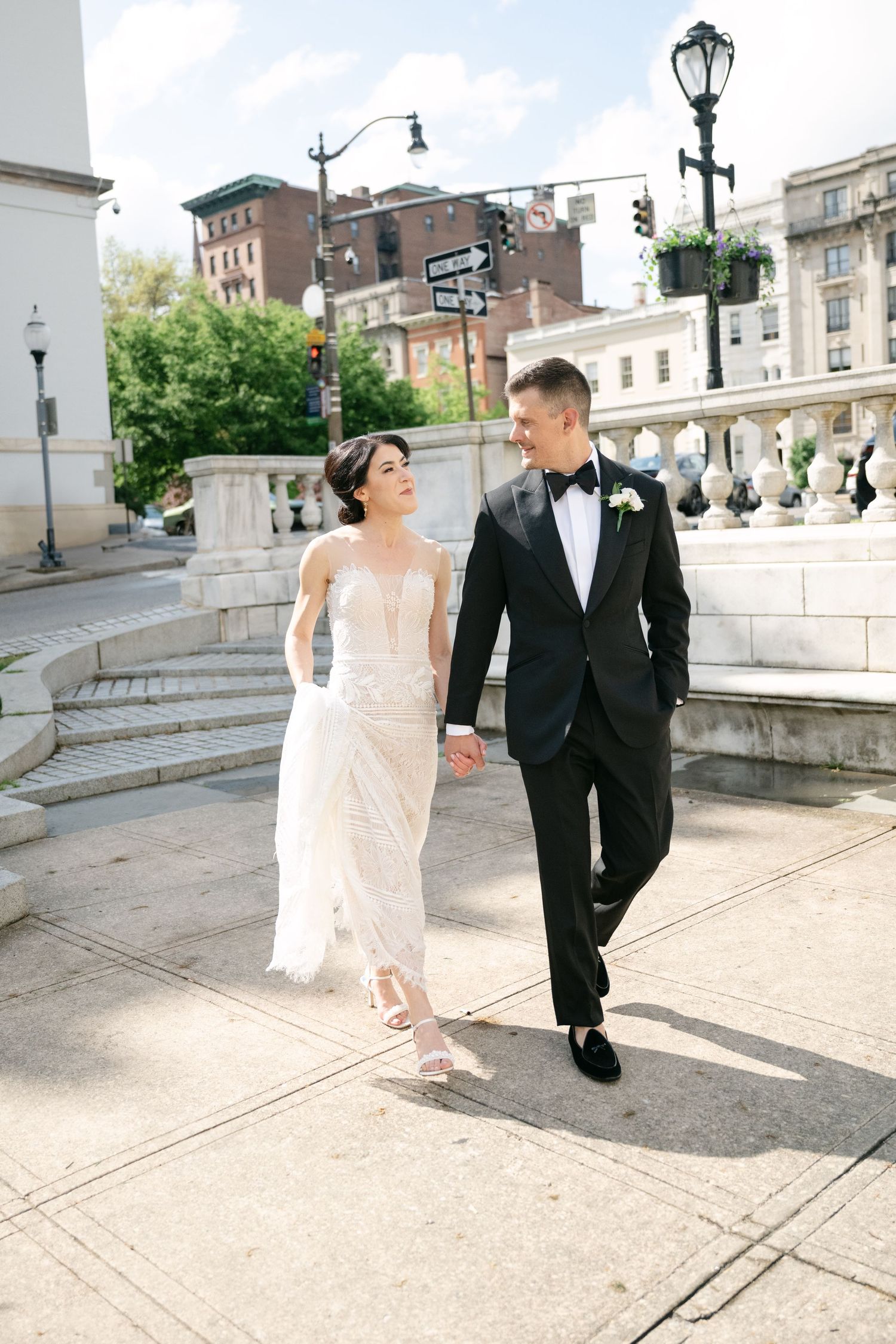 A couple walks together on an urban sidewalk with classic architecture and lamp posts in the background at a Baltimore engineers club
